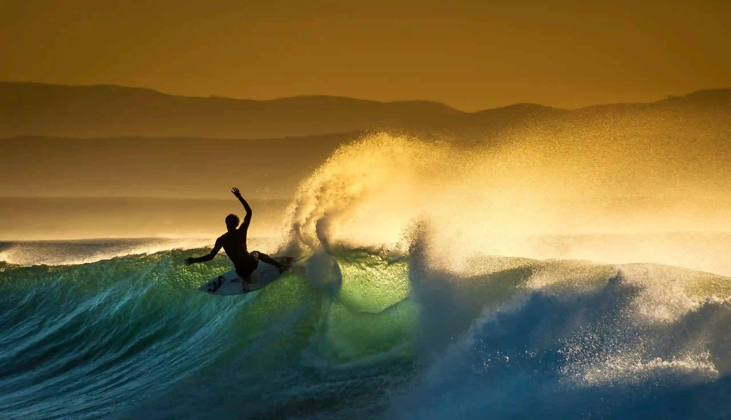 Ein Surfer reitet auf einer Welle im Sonnenuntergang.