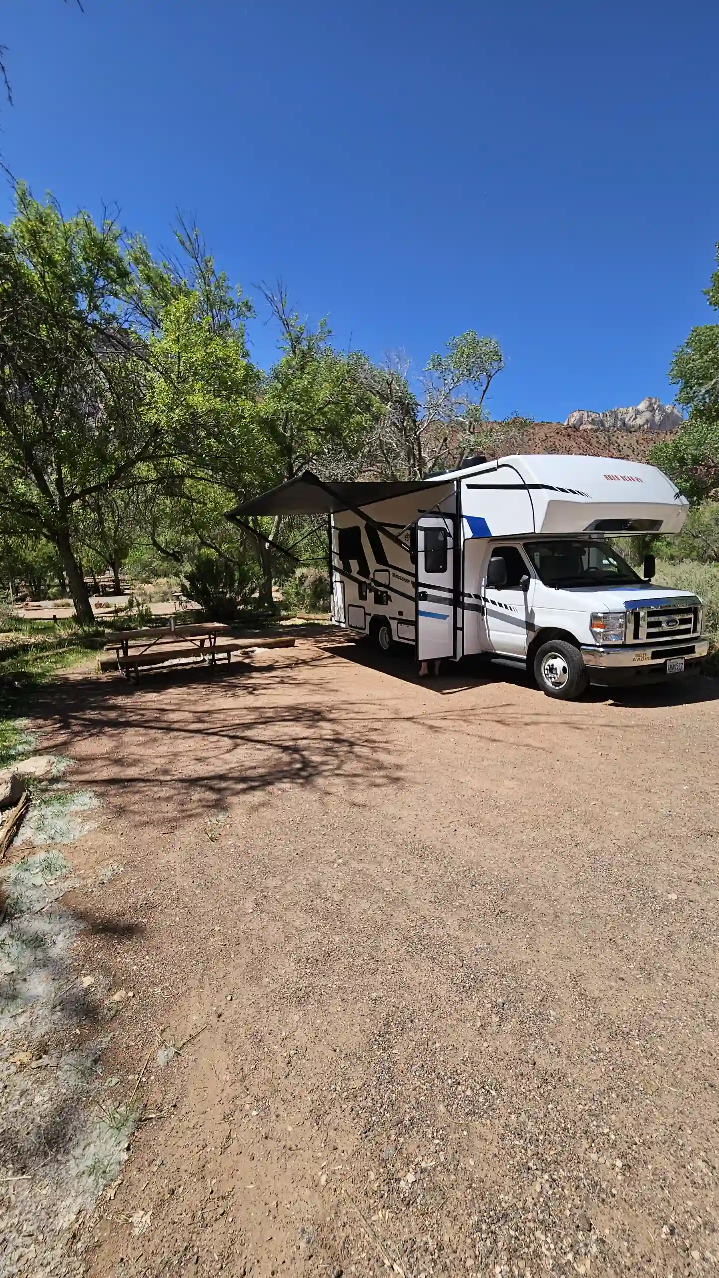 Ein Roadbear Camper steht auf sandigem Untergrund und von Bäumen umgeben.