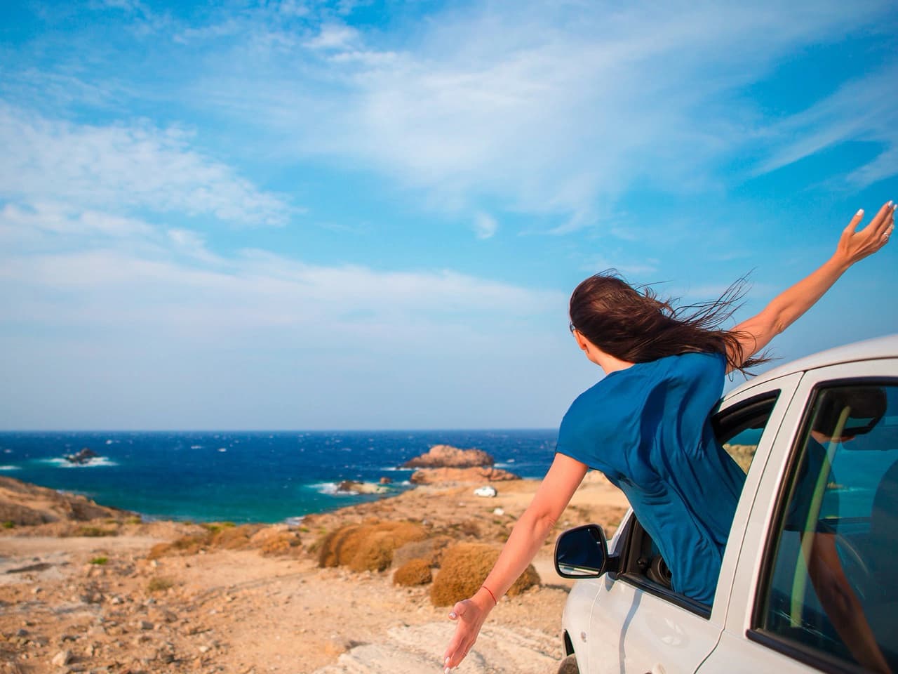 Frau lehnt sich aus dem Camper und blickt aufs Meer.