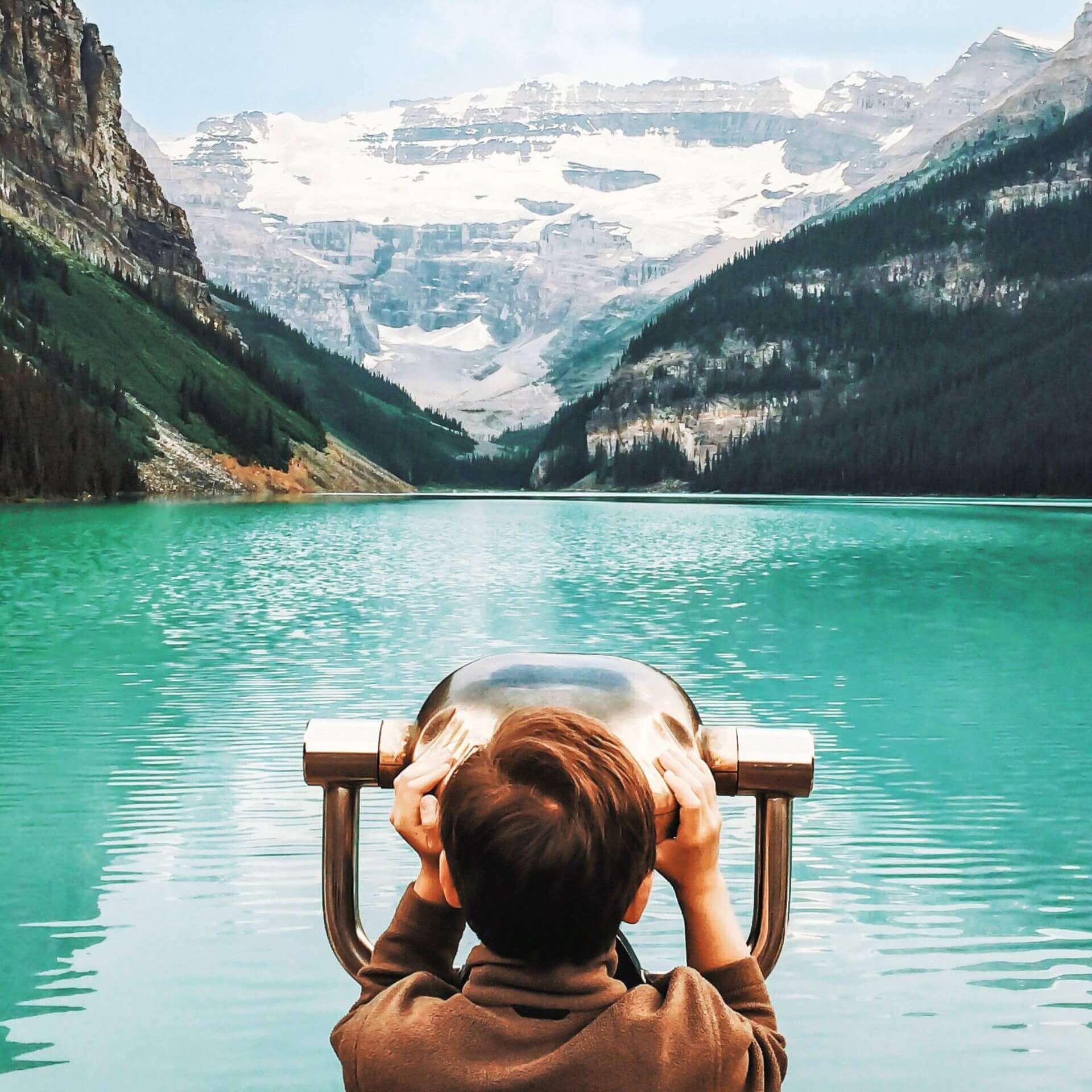 Ein Junge schaut durch ein Fernglass am Lake Louise