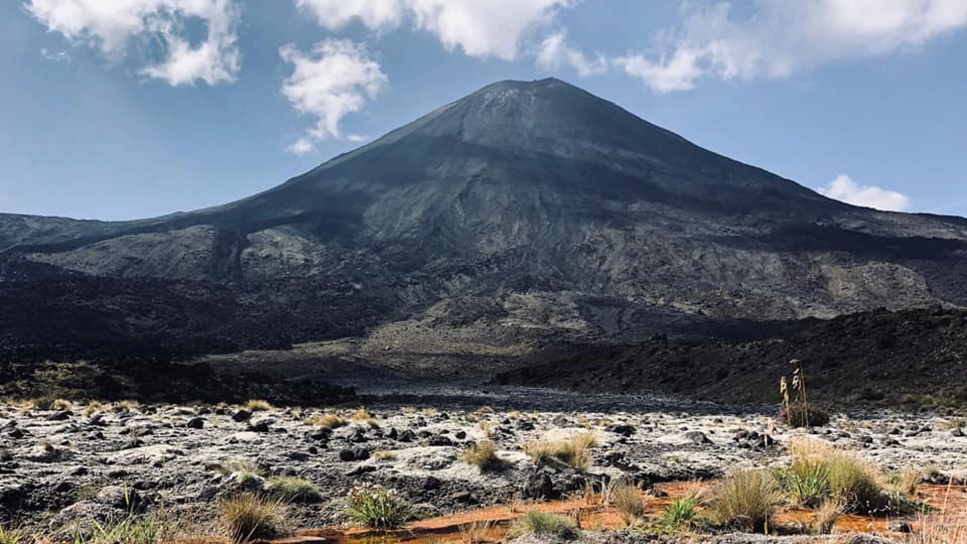 Blick auf einen Berg in Neuseeland mit Wolken und blauem Himmel im Hintergrund.