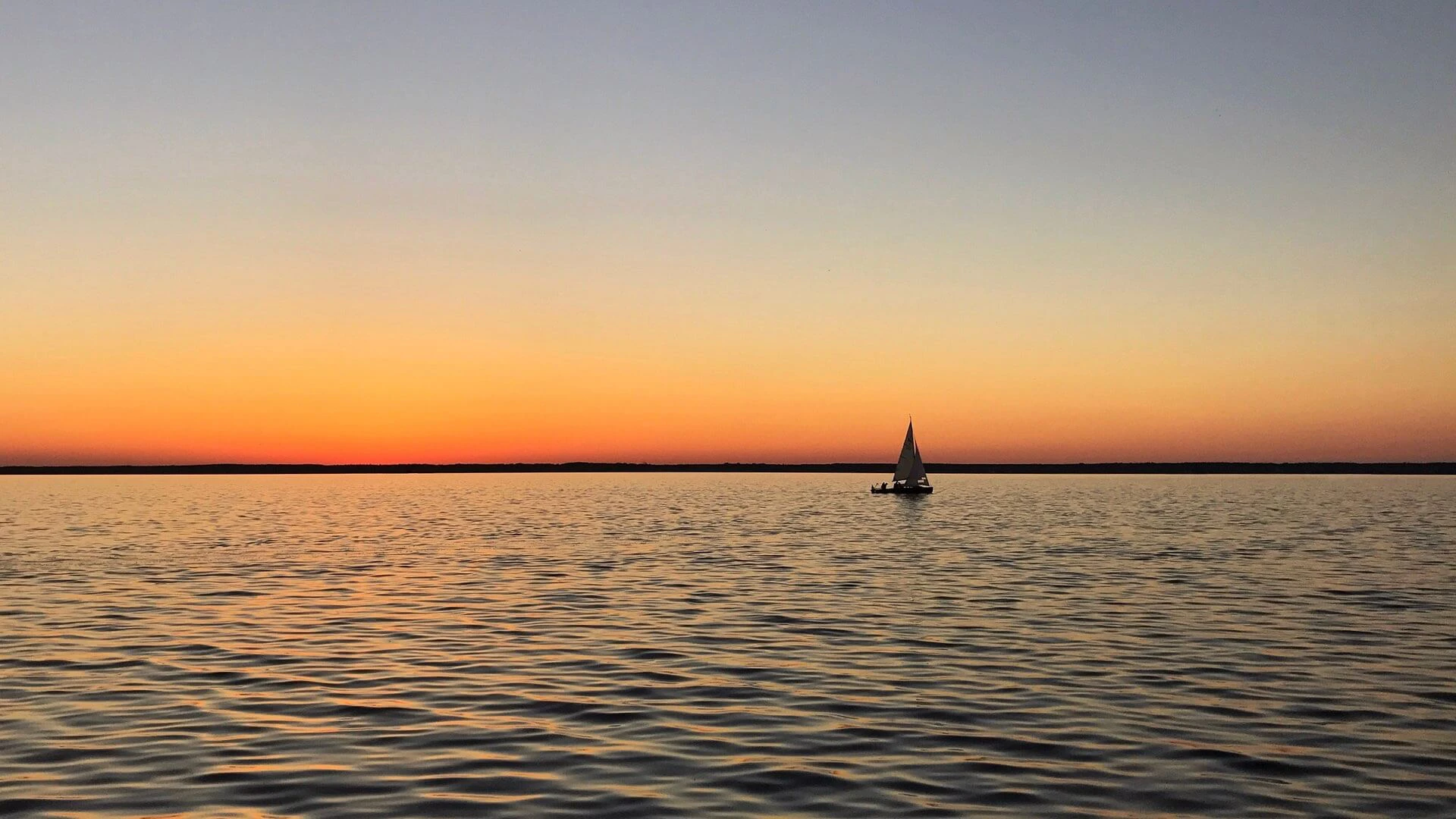 Ein kleines Segelboot auf dem Steinhuder Meer beim Sonnenuntergang.