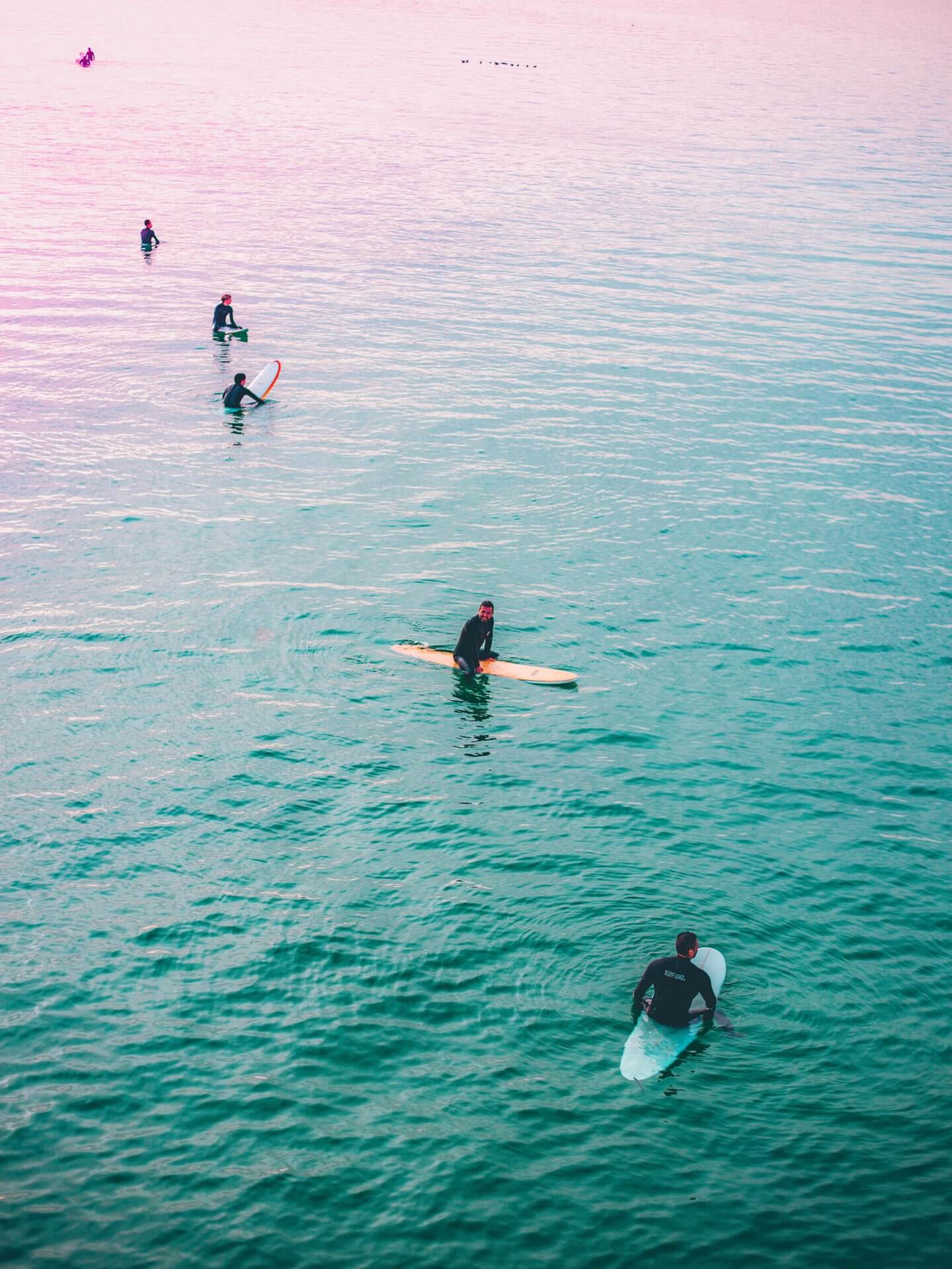 Mehrere Surfer sitzen auf ihrem Surfbrett im Wasser und warten auf die nächsten Wellen.