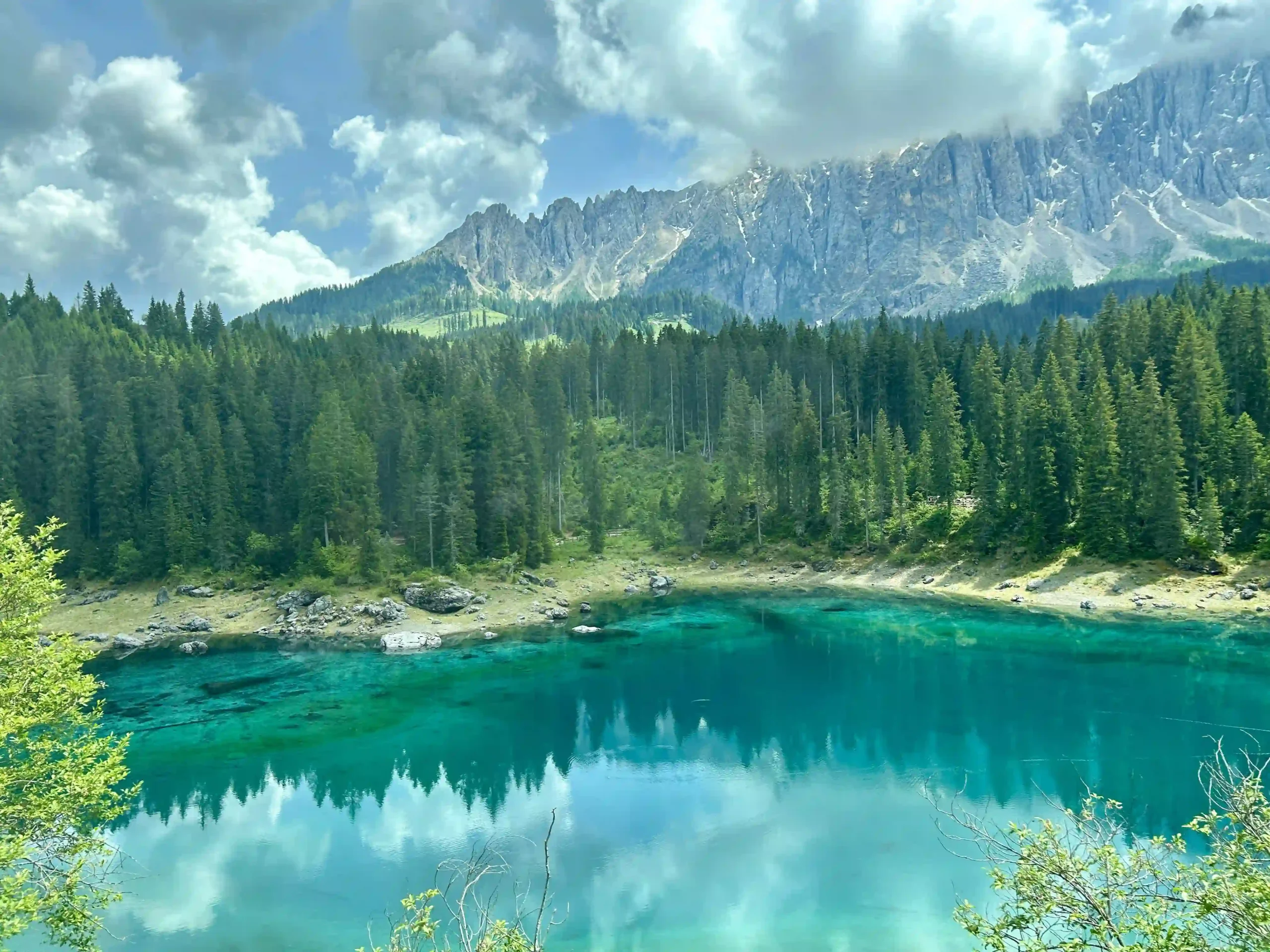 Ein glasklarer, türkiser See, umrahmt von dunkelgrünen Tannen mit Bergen im Hntergrund.