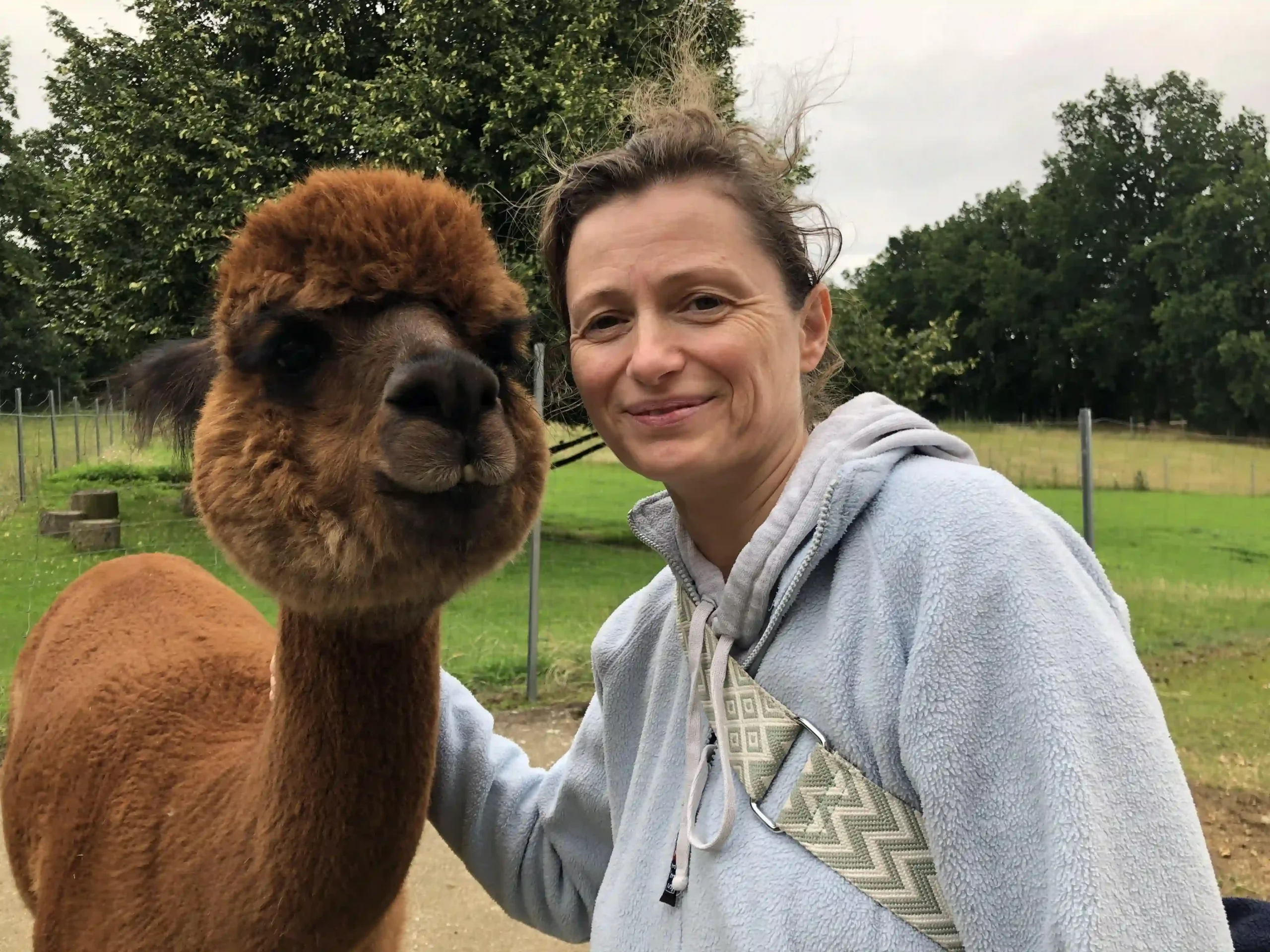 Ein Selfie einer lächelnden Frau neben einem flauschigen, braunen Alpaka.