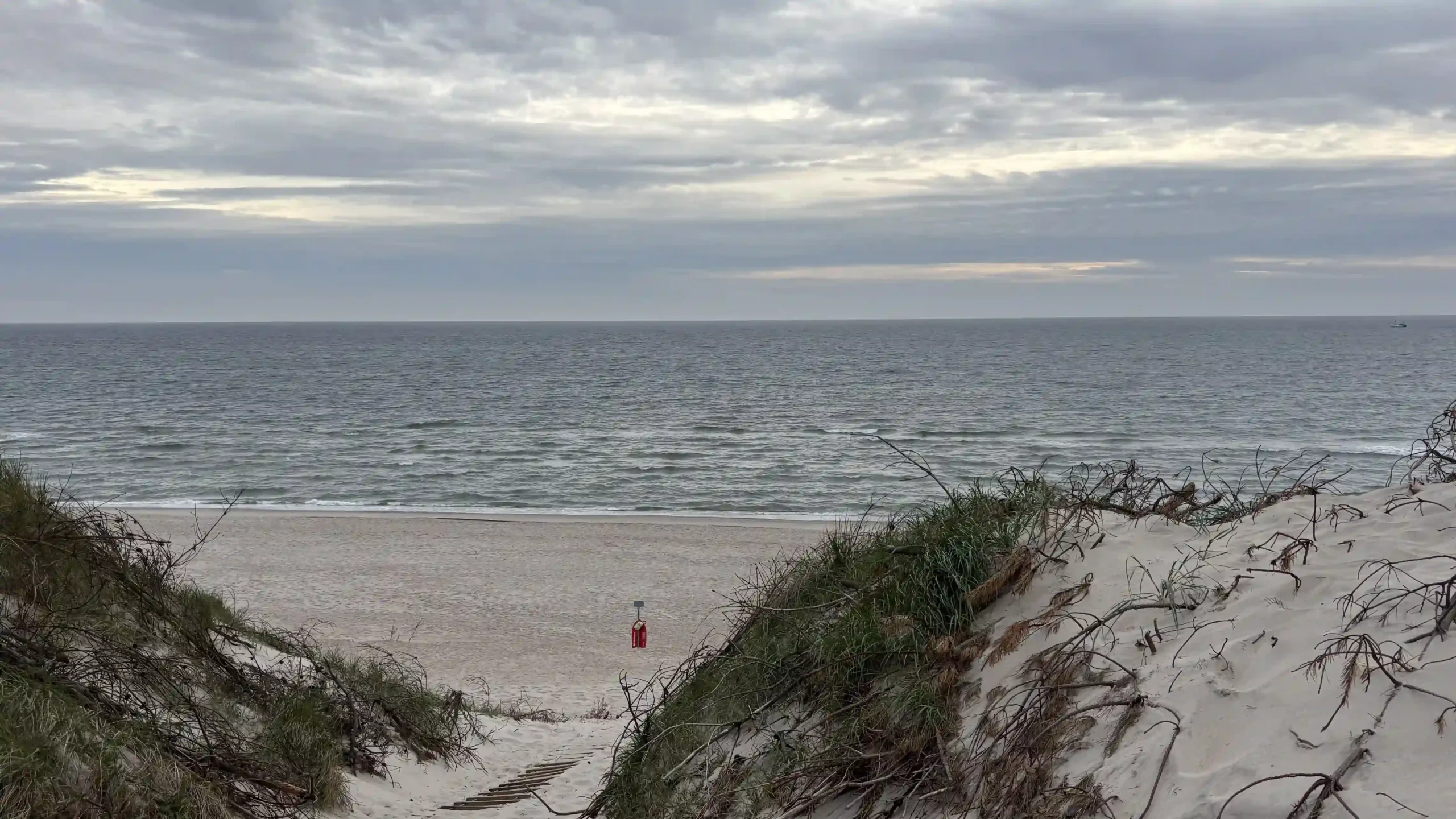 Weitwinkelaufnahme eines Dünendurchgangs mit Blick auf Strand und Meer.