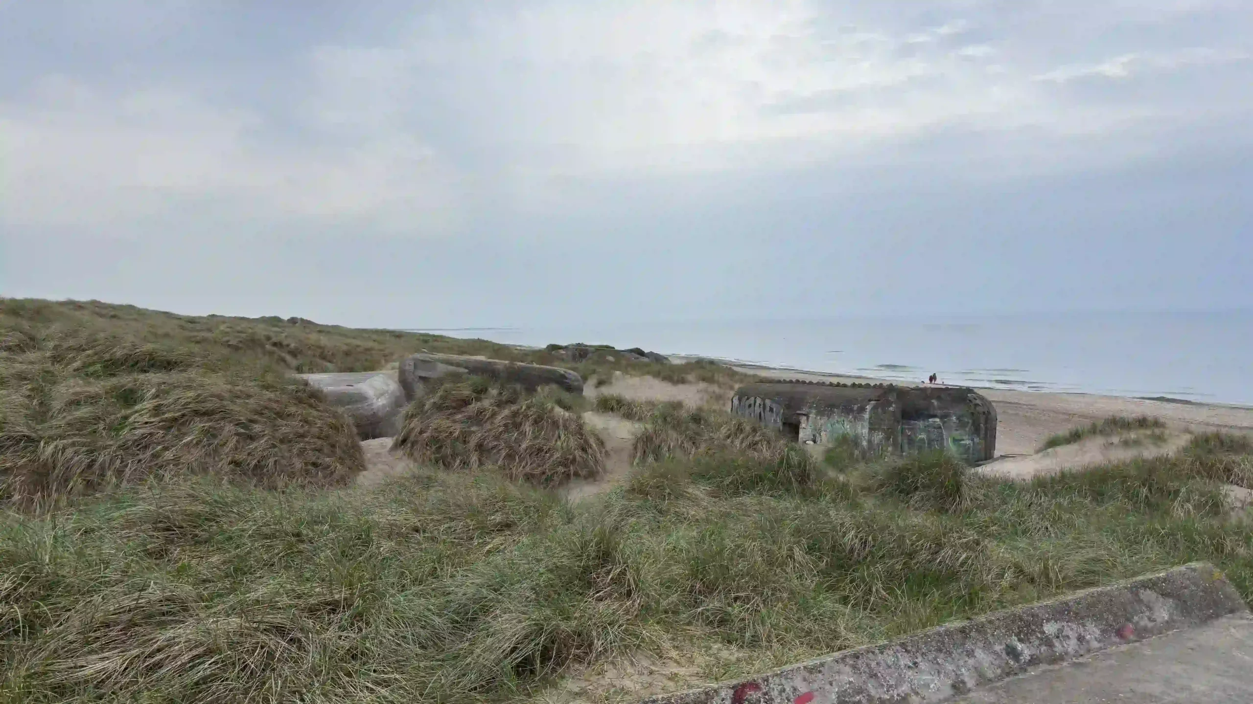 Mehrere verfallene Betonbunker aus dem Zweiten Weltkrieg sind in die grasbewachsenen Dünen eingebettet mit Blick aufs Meer.