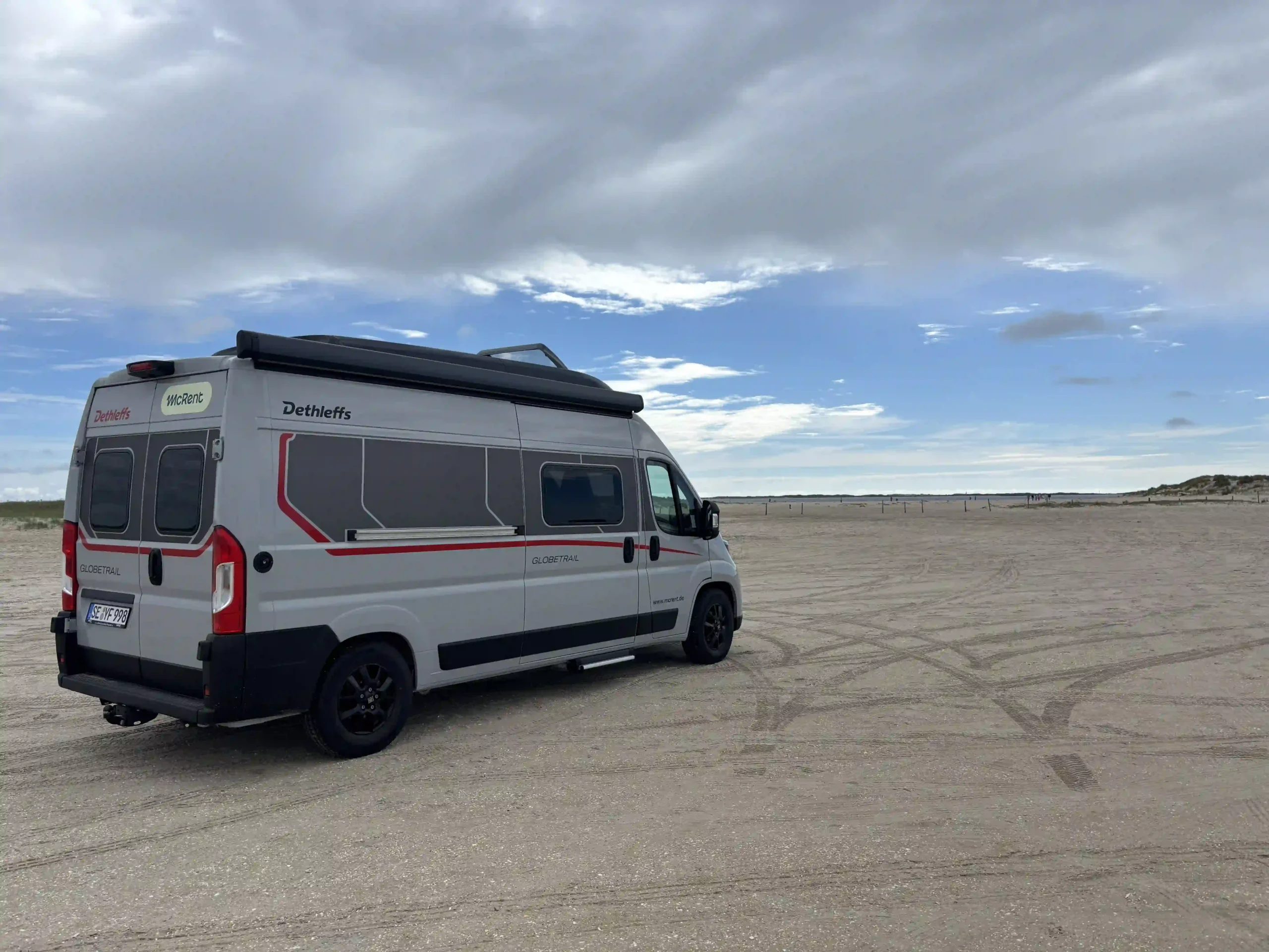 Aufnehme von einem Wohnmobil welches mitten auf einem kilometerbreiten, flachen Sandstrand in Dänemark parkt.