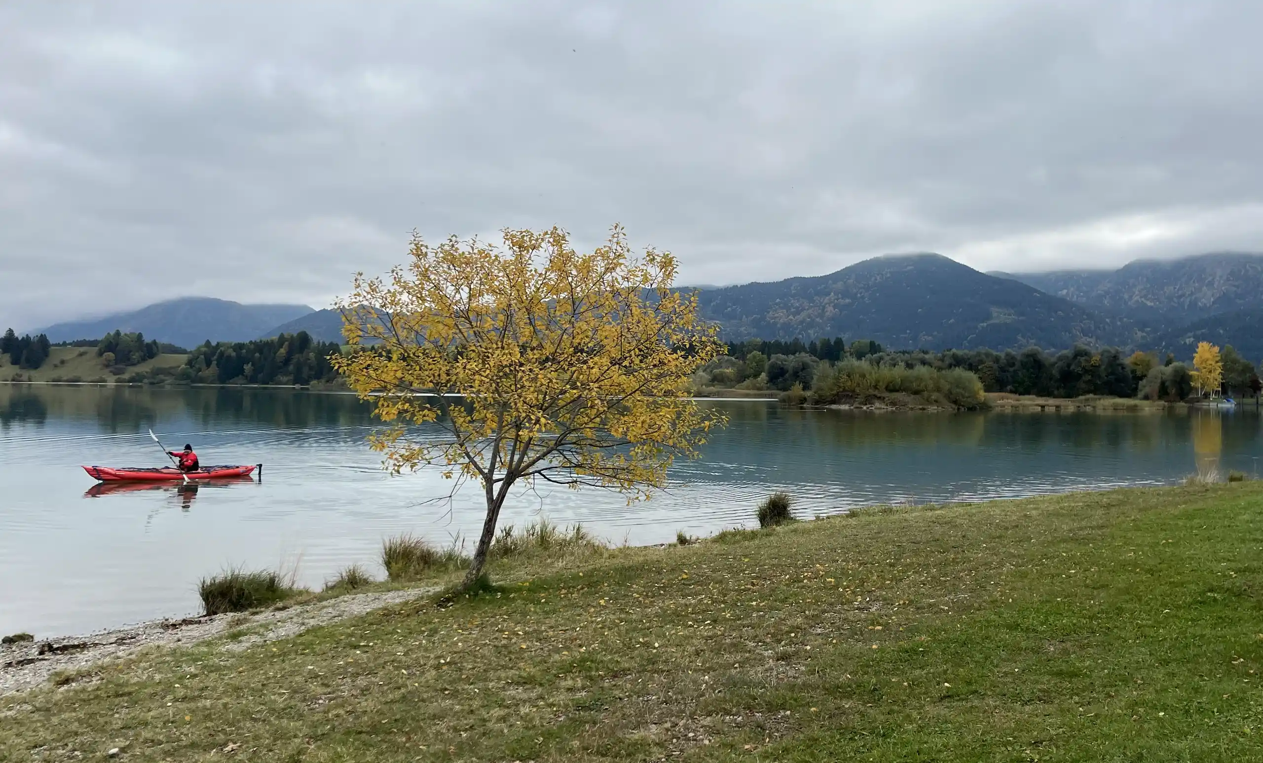 Blick auf den Forggensee im Süden Deutschlands bei bewölktem Himmel und einem Kanufahrer.