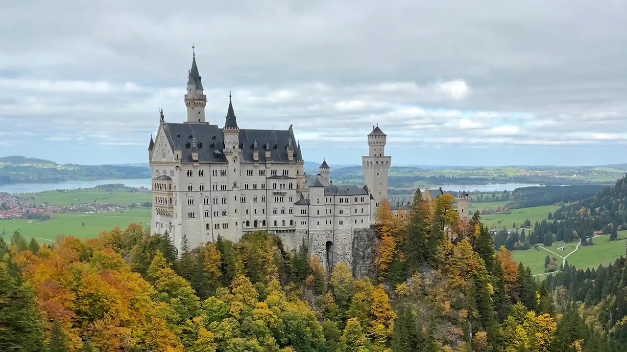 Blick auf das Schloss Neuschwanstein bei bewölktem Himmel und herbstlichem Wald.