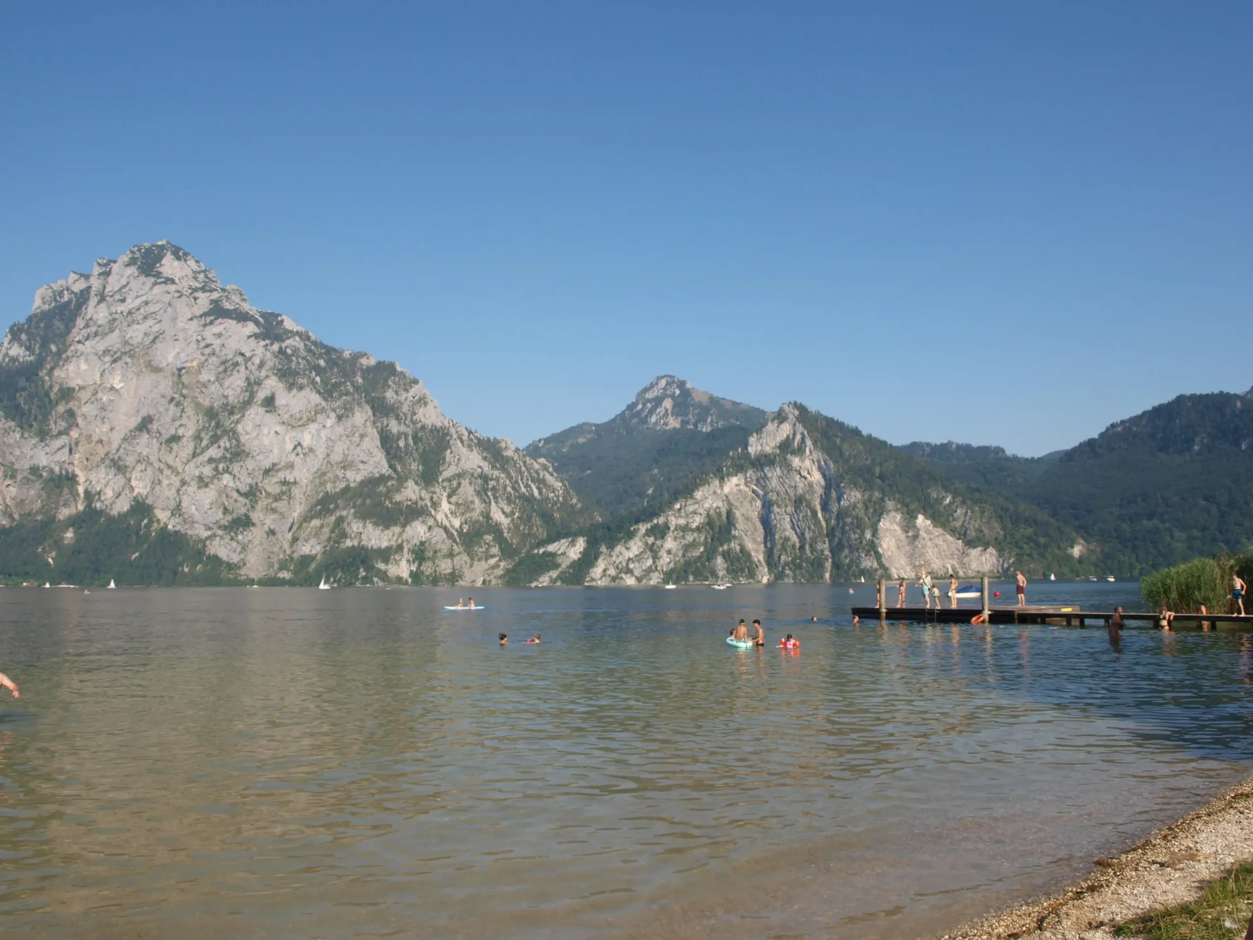 Ein sonniger Blick über einen klaren Badesee in den Alpen.