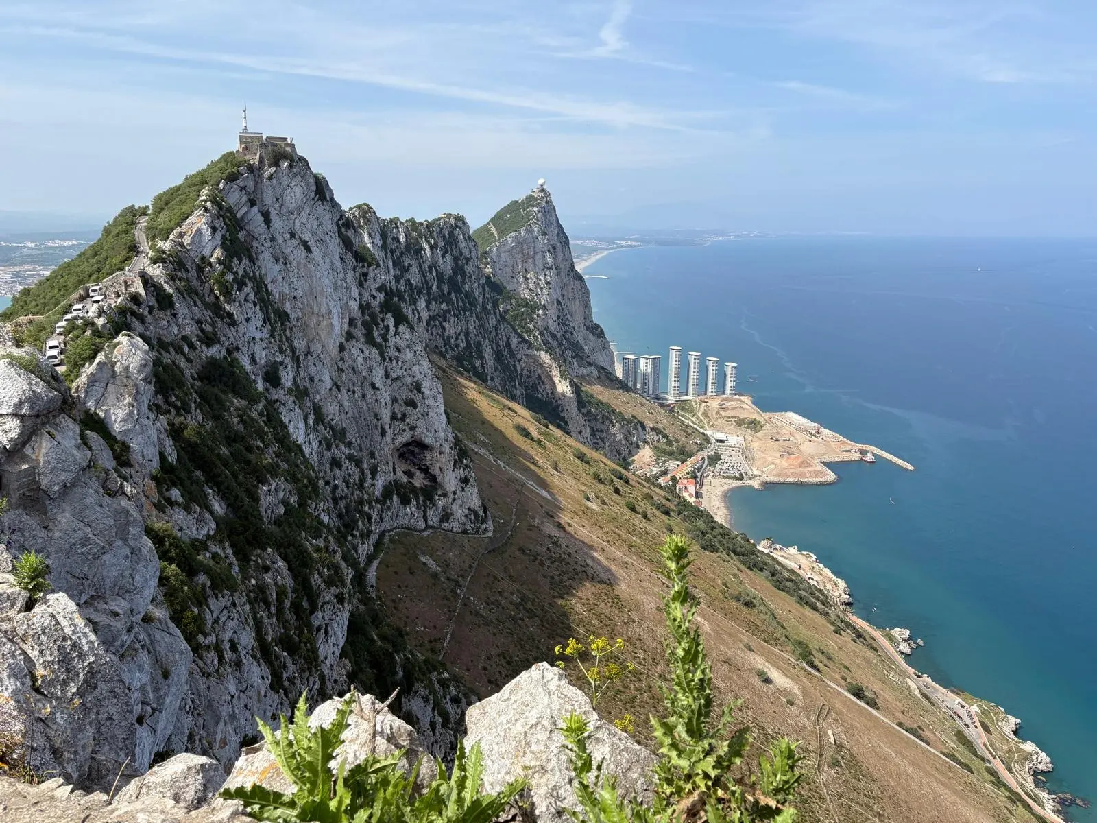 Blick von oben auf den markanten, steilen Kalksteinfelsen von Gibraltar. Auf der rechten Seite erstreckt sich das tiefblaue Meer.