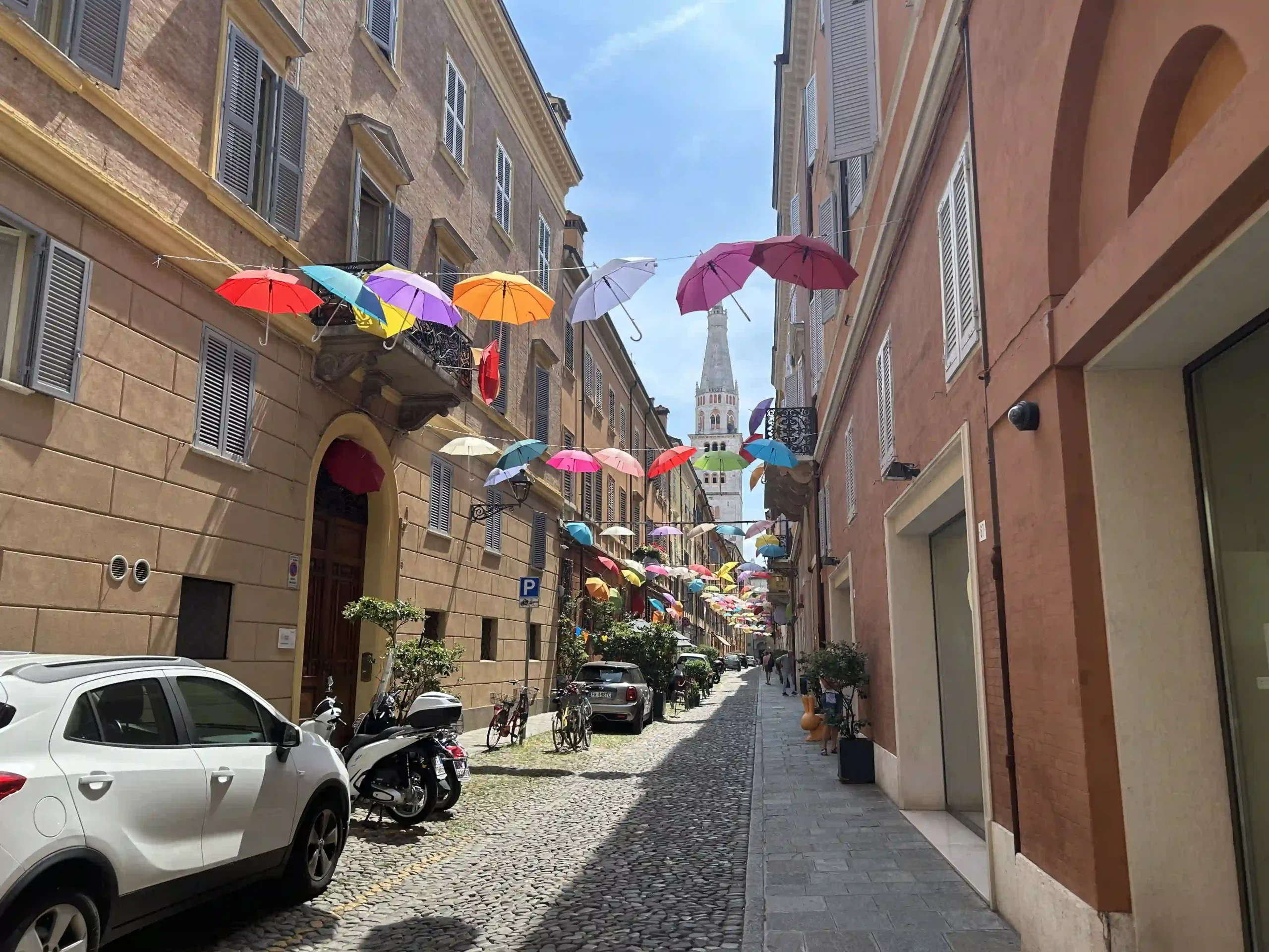 Eine kopfsteingepflasterte Gasse bei strahlend blauem Himmel, geziert mit bunten Regenschirmen.
