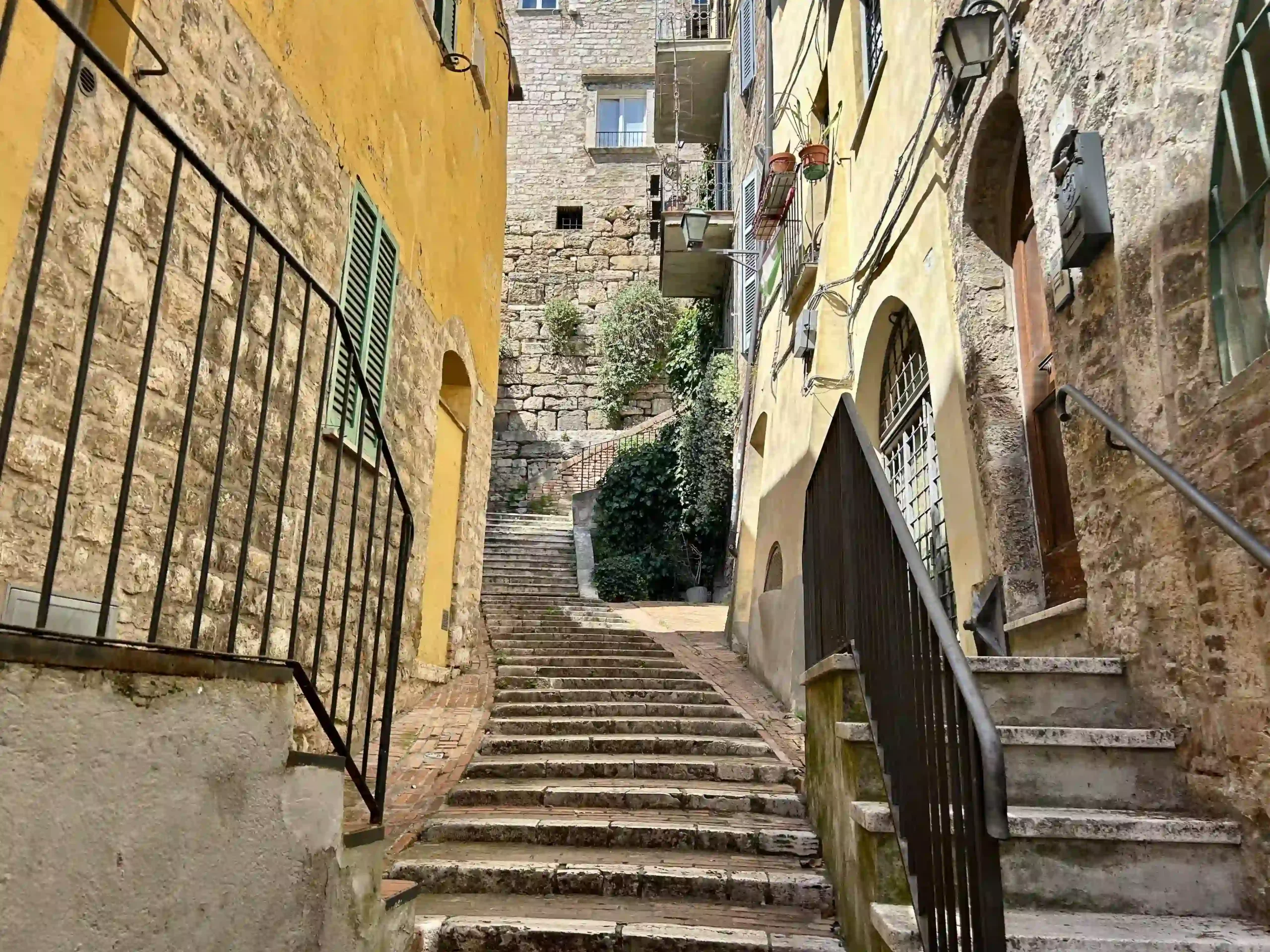 Eine aus Treppen bestehende Gasse, gesaeumt von alten, gelb getönten Häusern bei sonnigem Wetter.