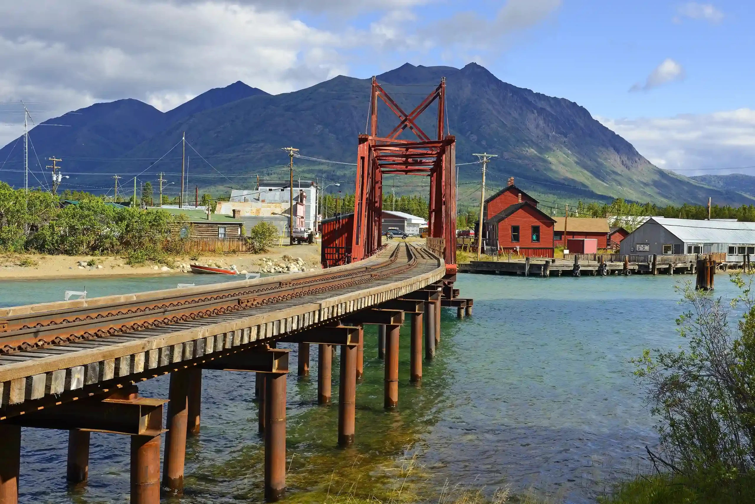 Eine rote Eisenbahnbrücke führt über einen hellblauen Fluss.