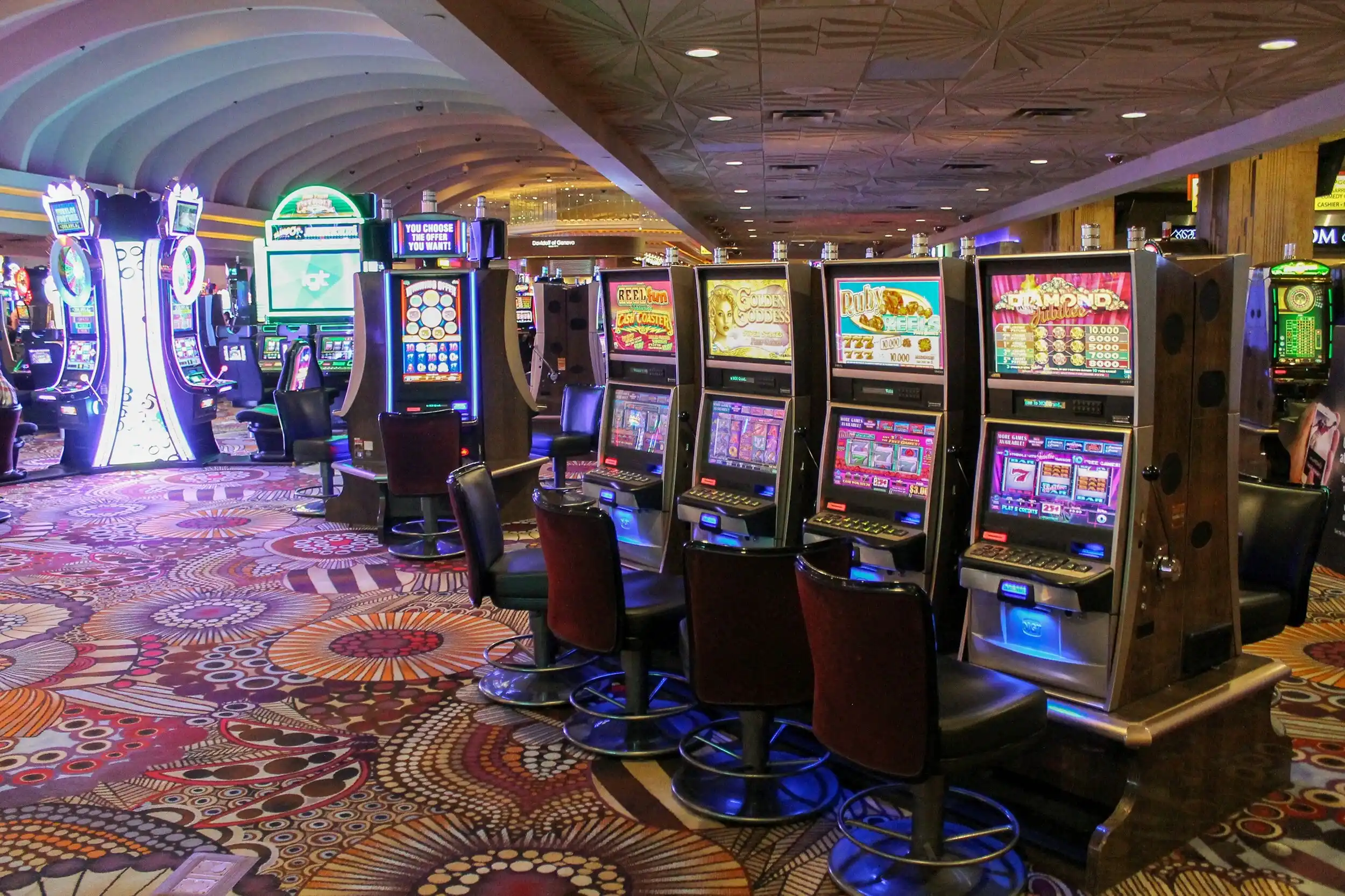Eine Reihe bunter Spielautomaten in einem Casino in Las Vegas mit gemustertem Teppich.