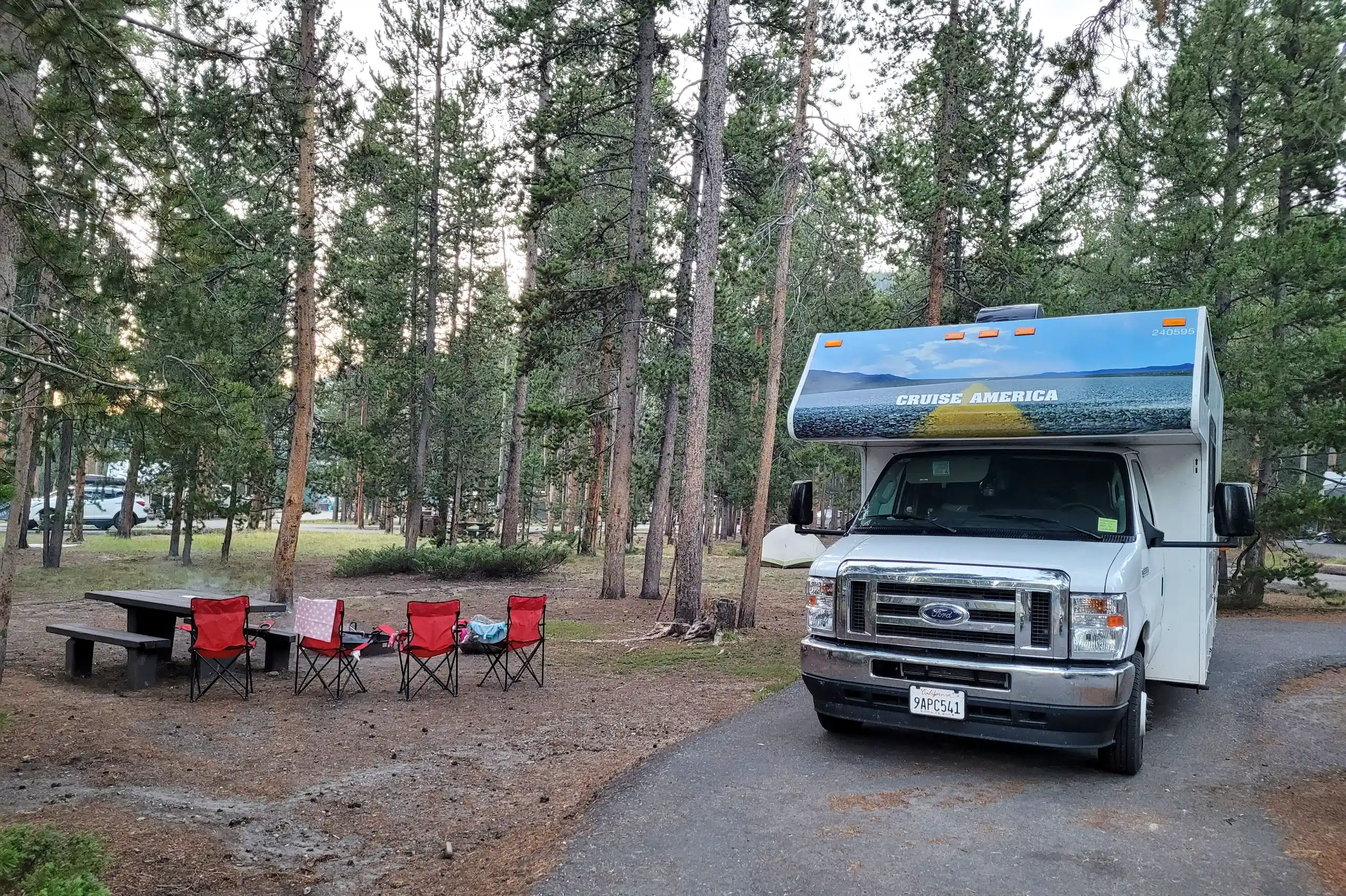 Ein Wohnmobil von Cruise America parkt auf dem Madison Campground neben einem Picknicktisch und -Stühlen im Yellowstone-Nationalpark