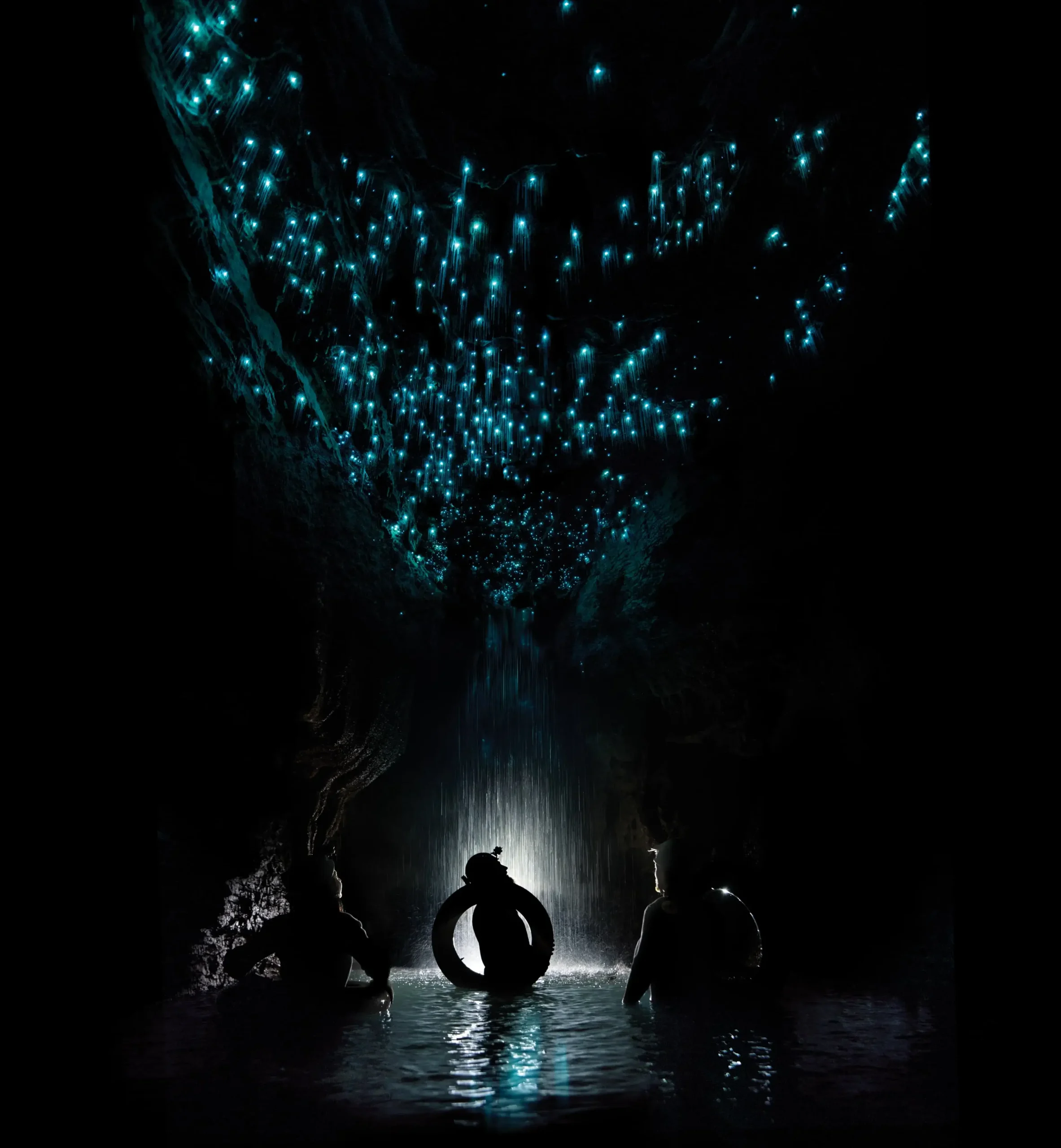 Die Silhouetten von drei Abenteurer, im Wasser, unter dem Glühwürmchen-Himmel von Waitomo.
