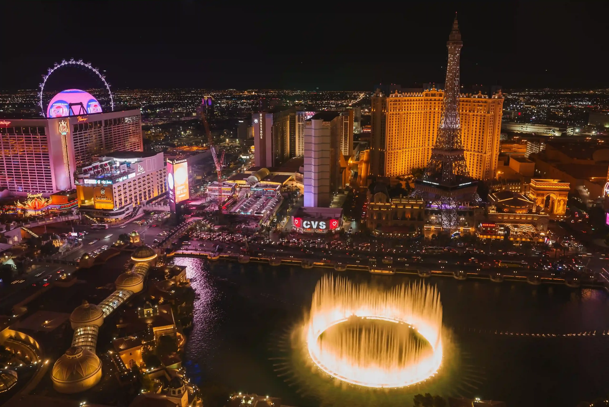 Nächtliche Skyline des Las Vegas Strip mit hell erleuchteten Hotels, Casinos und einer markanten Wasserfontäne im Zentrum.