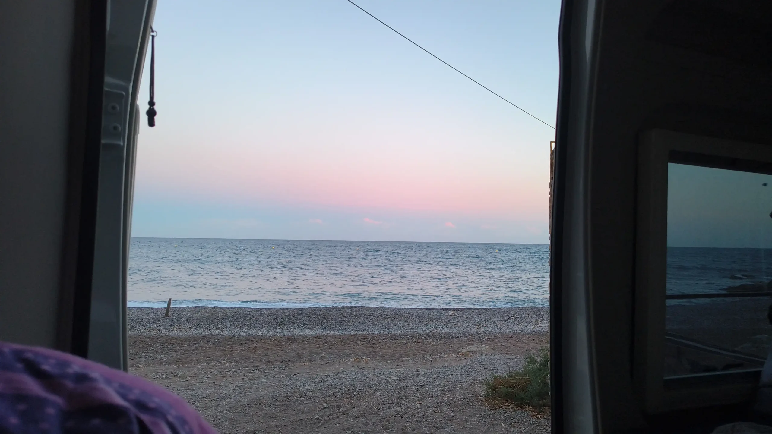Blick aus der geöffneten Schiebetür eines Wohnmobils direkt auf einen Kiesstrand und das offene Meer.
