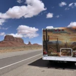 Die Rückansicht eines weißen "Cruise America"-Wohnmobils, das am rechten Rand einer asphaltierten Landstraße parkt.