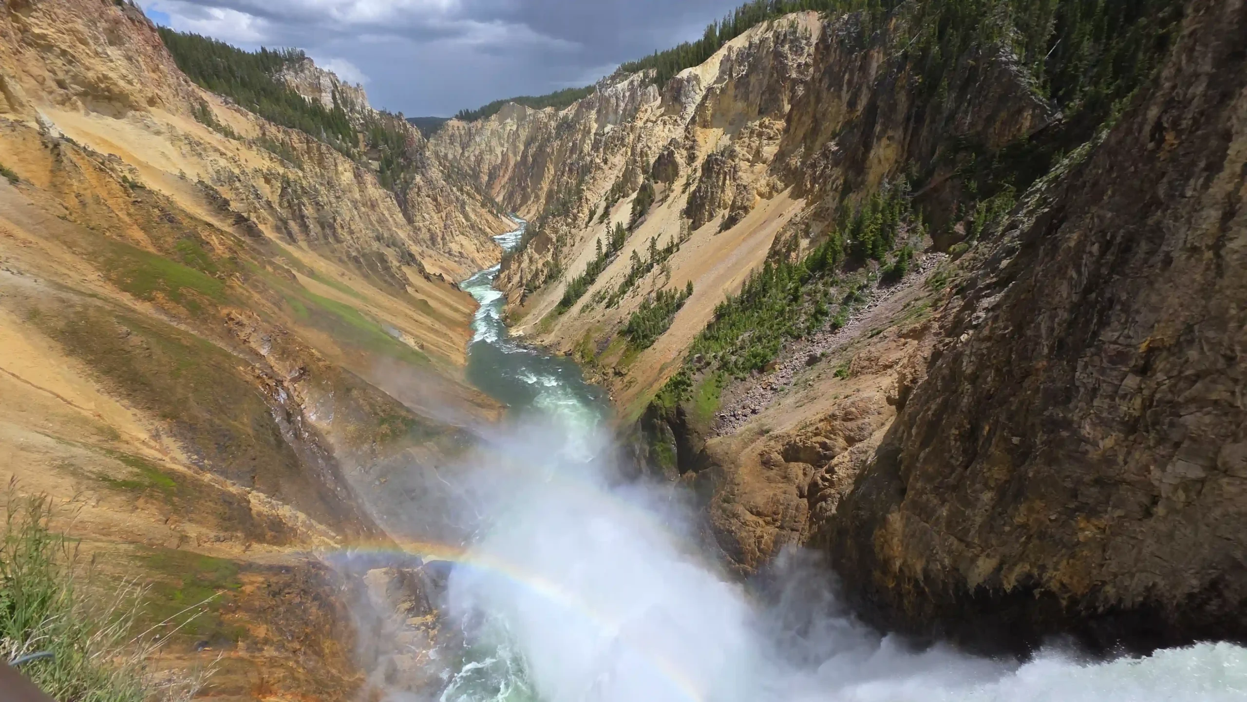 Ein Wasserfall sich stürzend in die tiefe Schlucht des Grand Canyons, wo er als Fluss in den Horizont fließt. Im Nebel des Wasserfalls reflektiert ein Regenbogen.