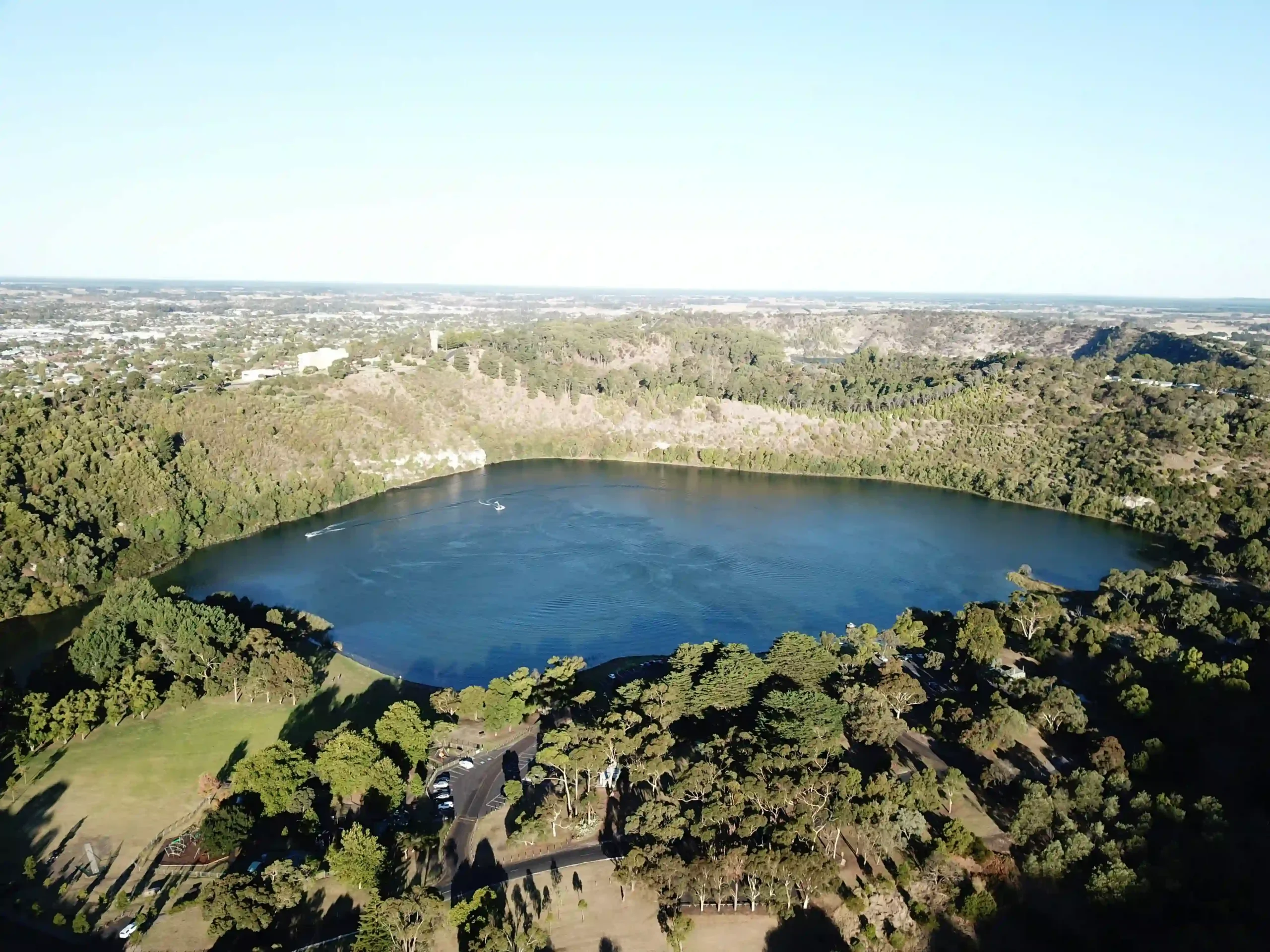 Aerial view of a large, deep blue crater lake surrounded by steep, tree-covered limestone walls.