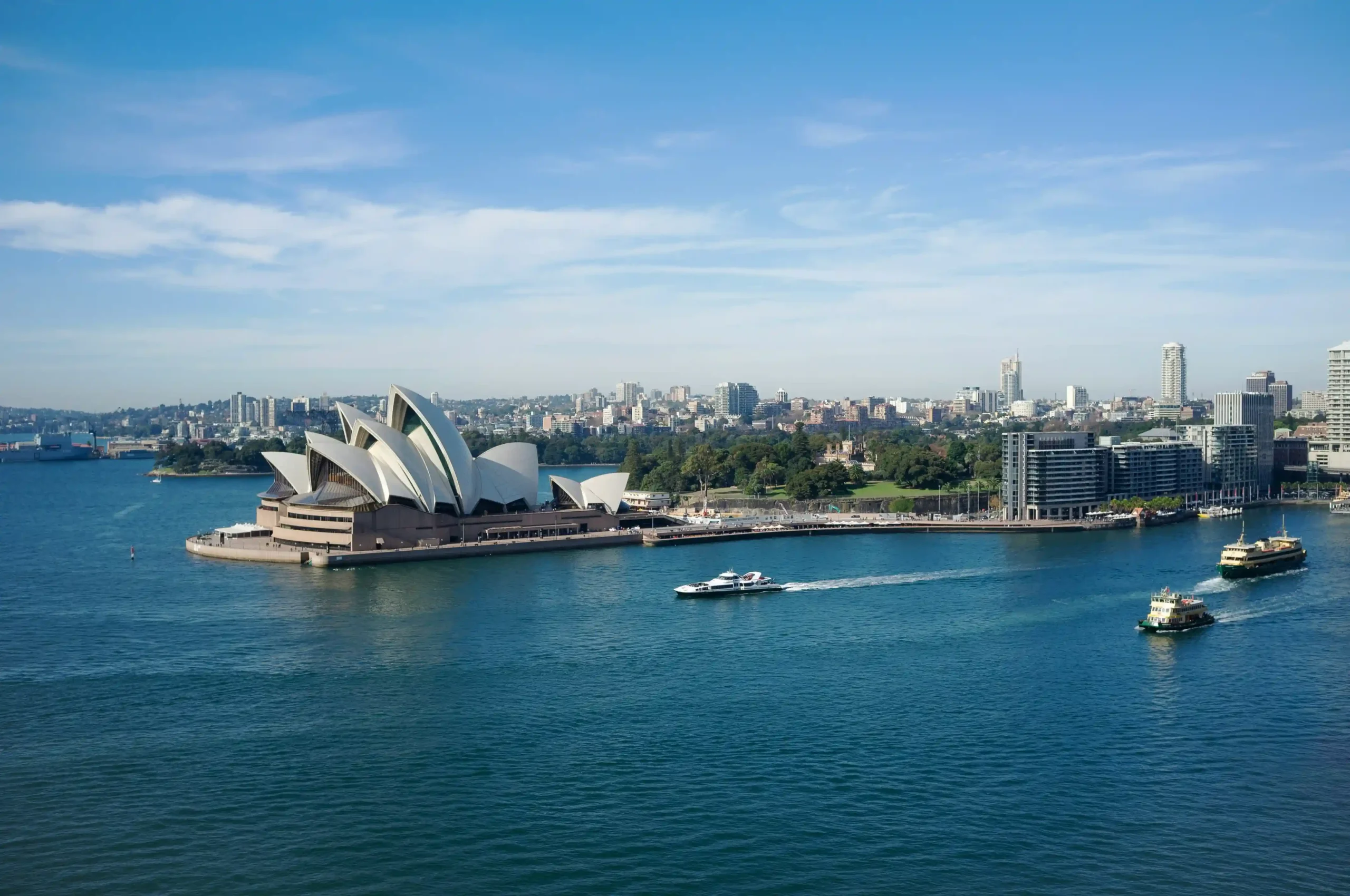 Vew of the Sydney Opera House sitting on a peninsula surrounded by deep blue water.