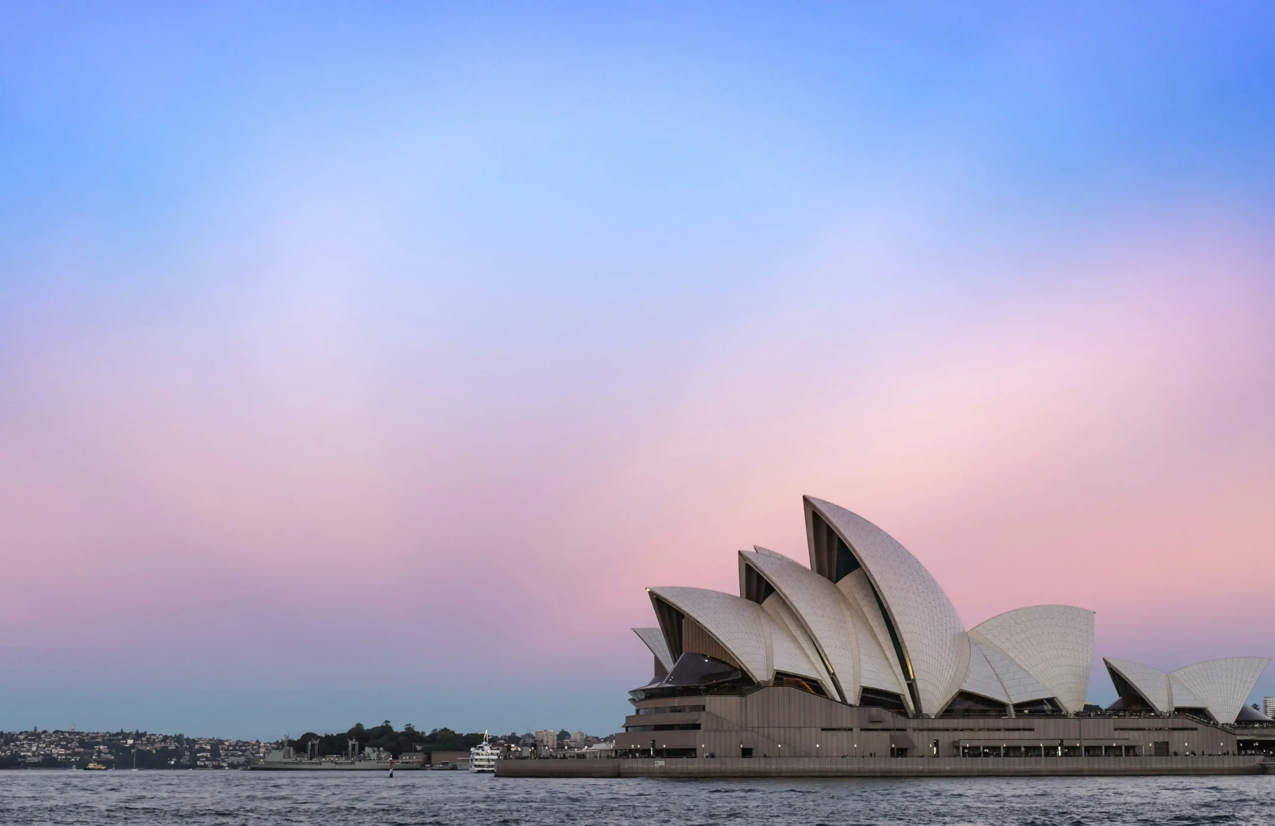 The white sails of Sydney’s Opera House stand out against a soft purple and pink gradient sky.