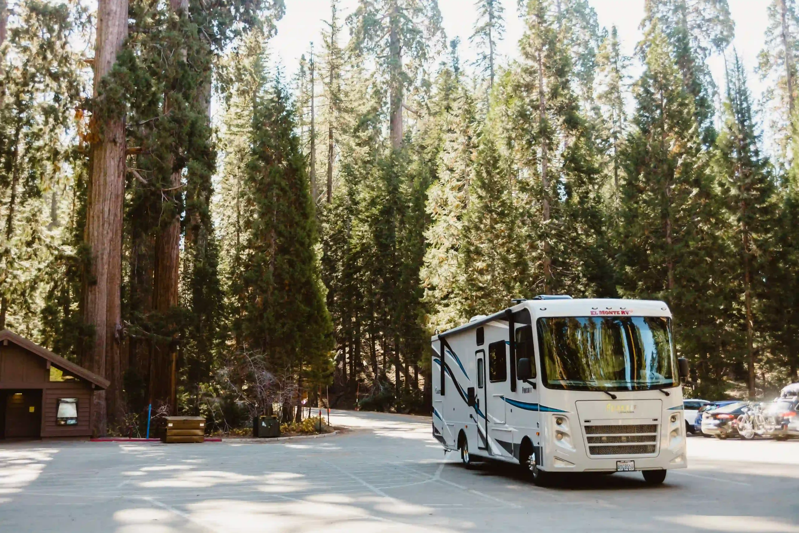 A large white Class A motorhome parked in a paved lot surrounded by trees.