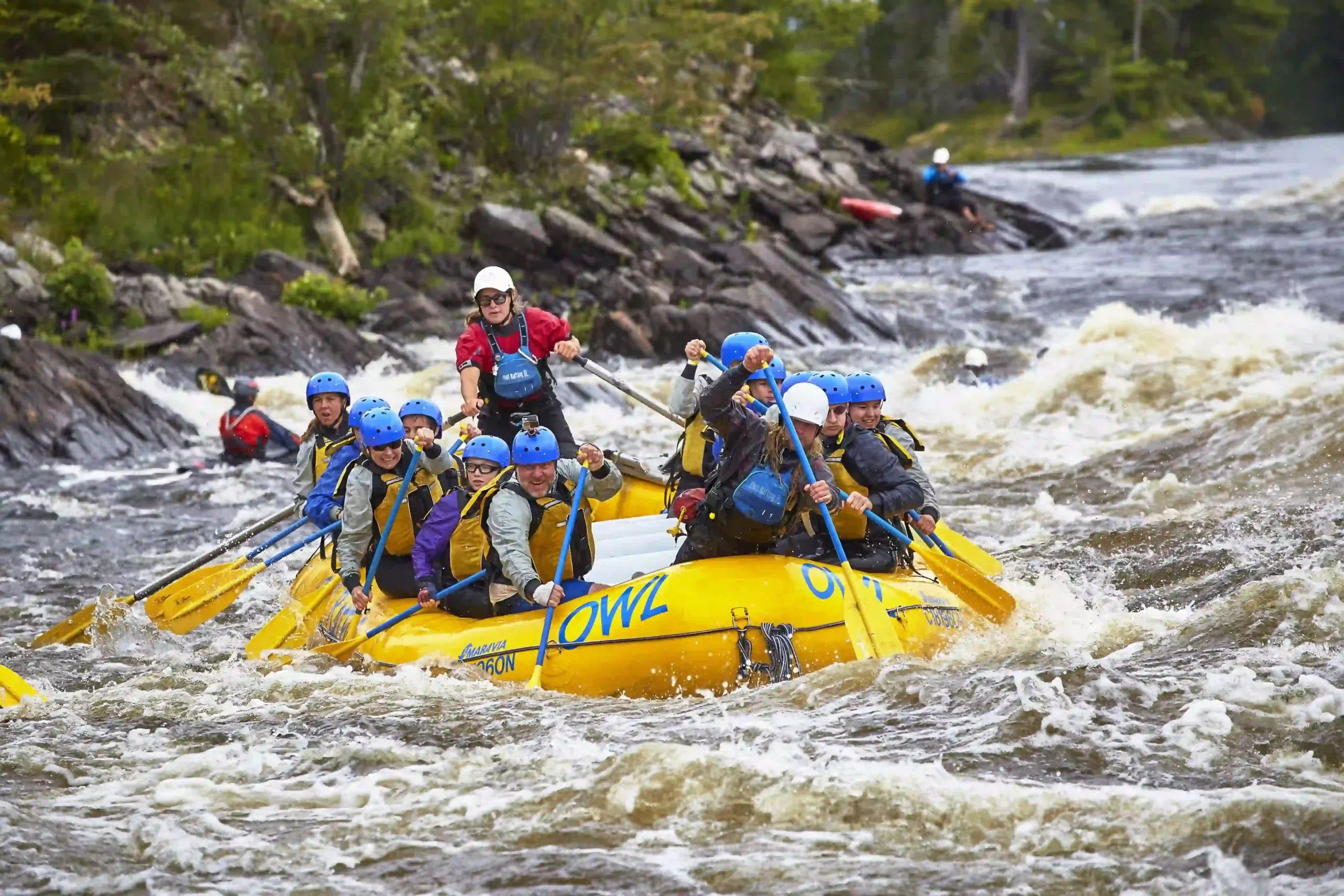 A group of people in blue helmets and yellow life jackets paddling a bright yellow \