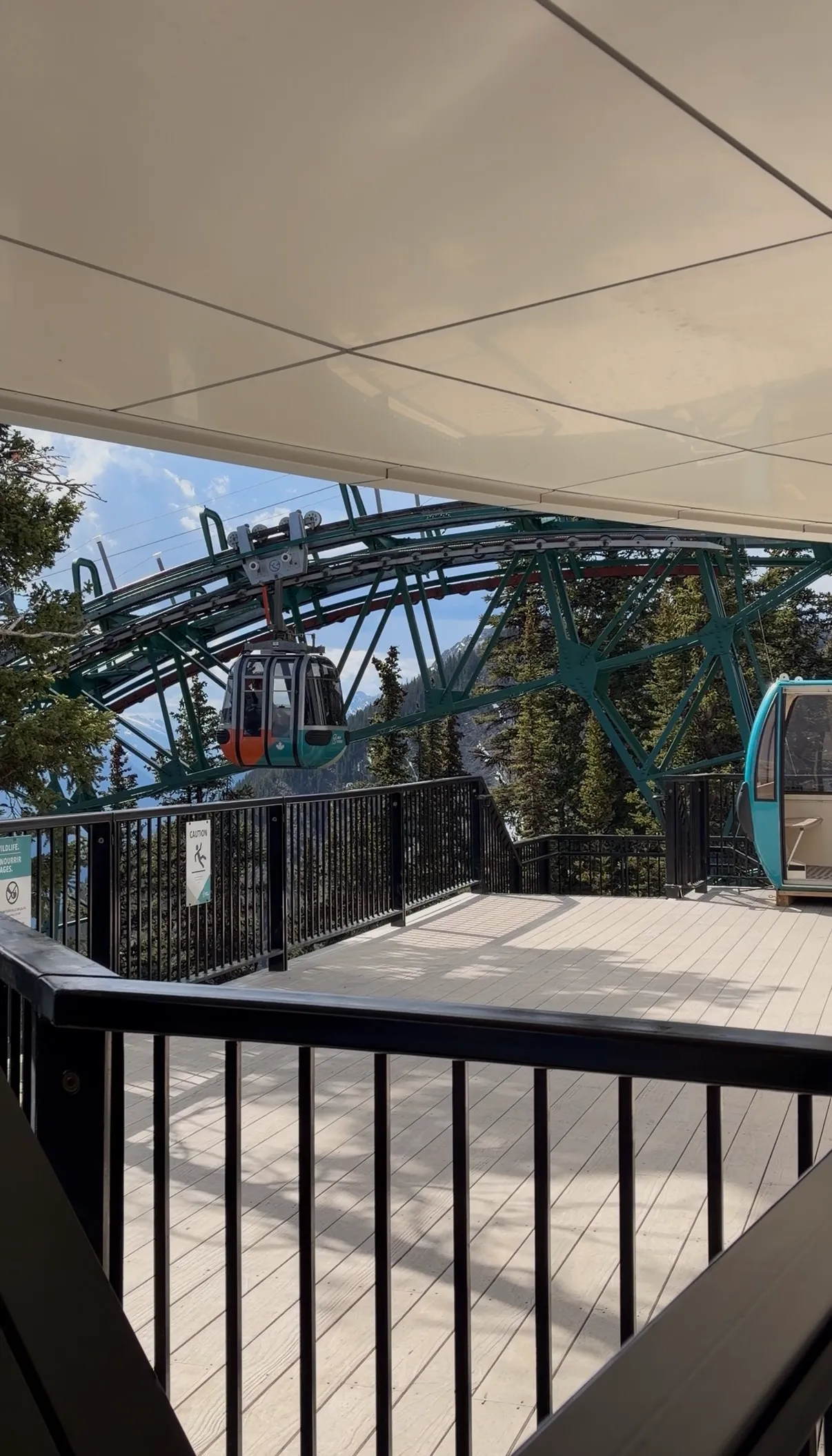 An orange gondola car traveling on a green metal track above a wooden observation deck.
