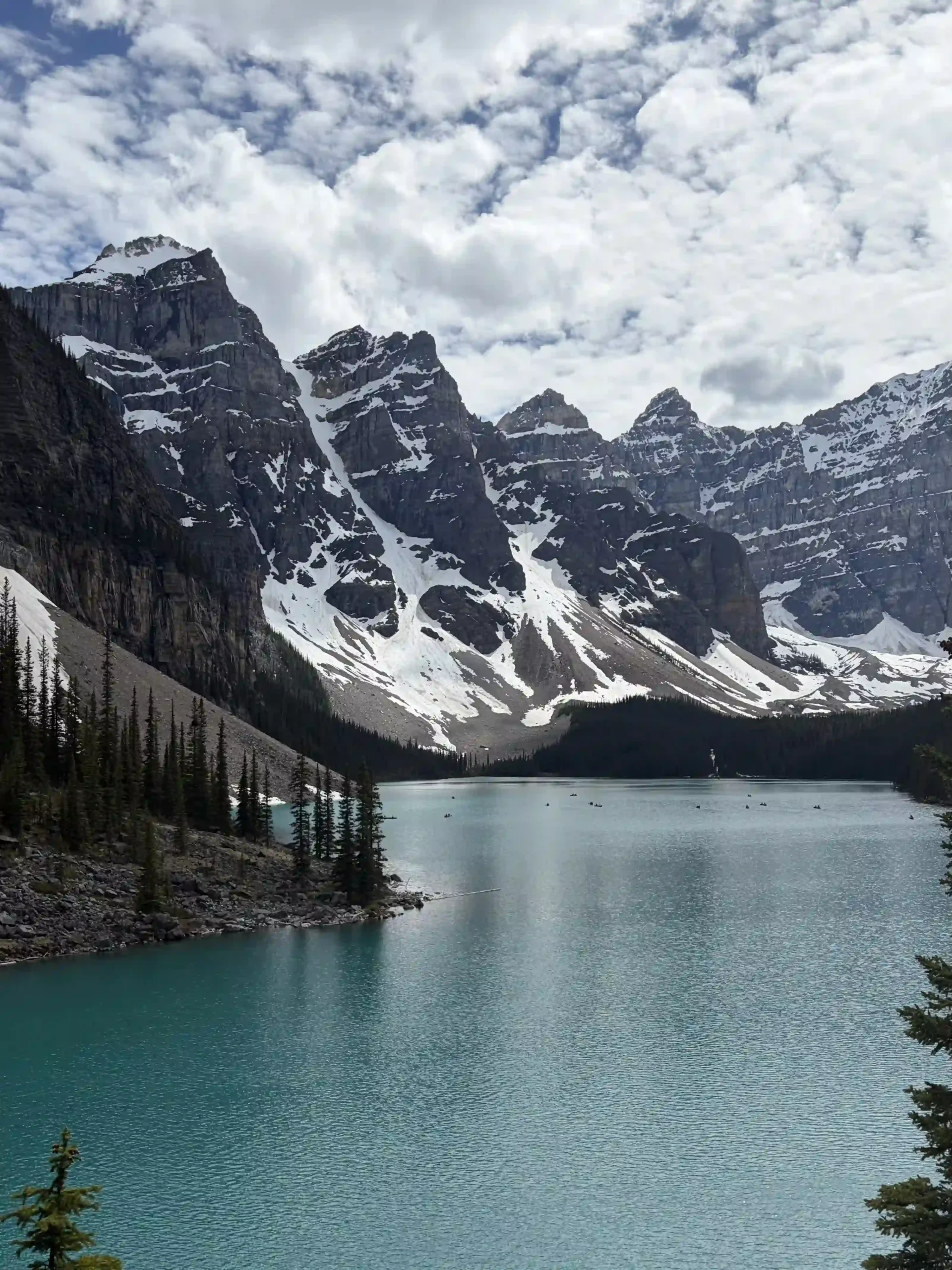 Panoramic view of the vibrant turquoise waters of Moraine Lake surrounded by snow-dusted, rugged mountain peaks.