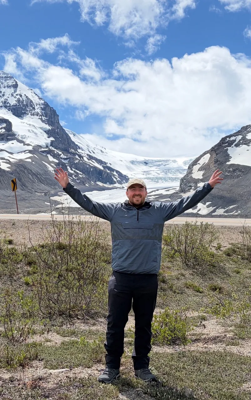 A traveler smiling with open arms in front of the sweeping view of the Columbia Icefield.