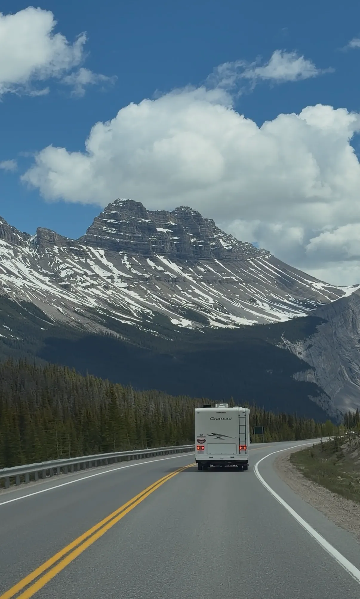 A motorhome cruising along the scenic Icefields Parkway near the Columbia Icefield in Jasper National Park. Mountain peaks frame the route.