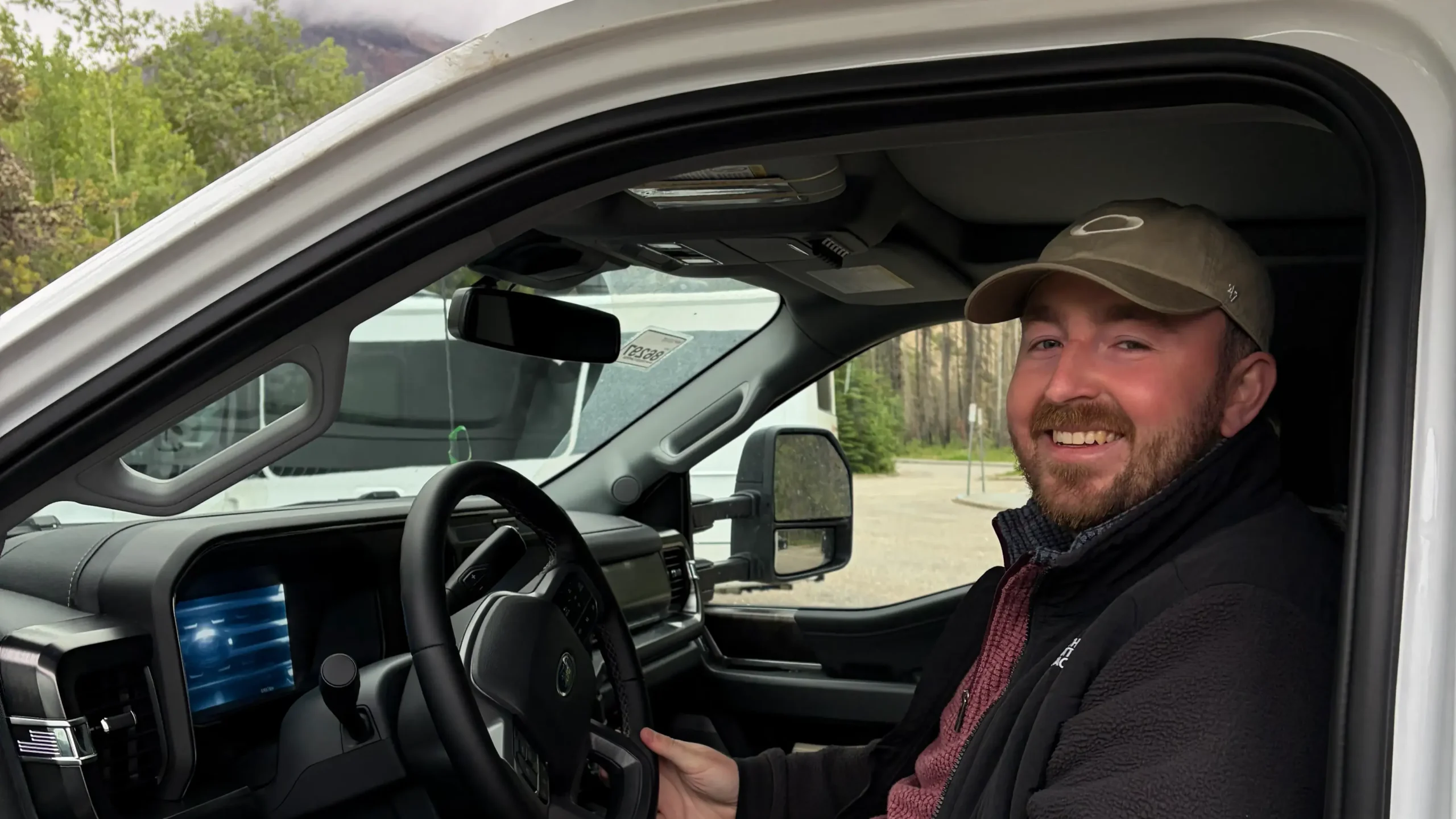 A cheerful road tripper sitting in the driver\'s seat of a white motorhome.