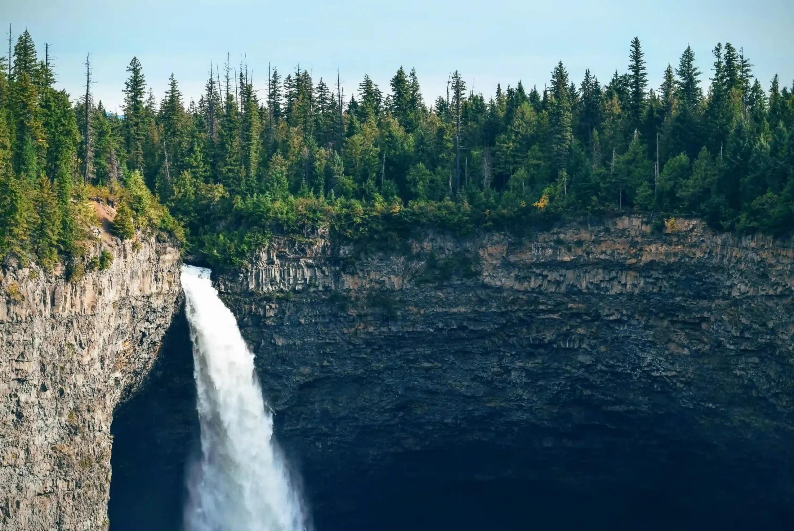 A massive white waterfall plunging over a sheer basalt cliff into a deep, dark canyon.