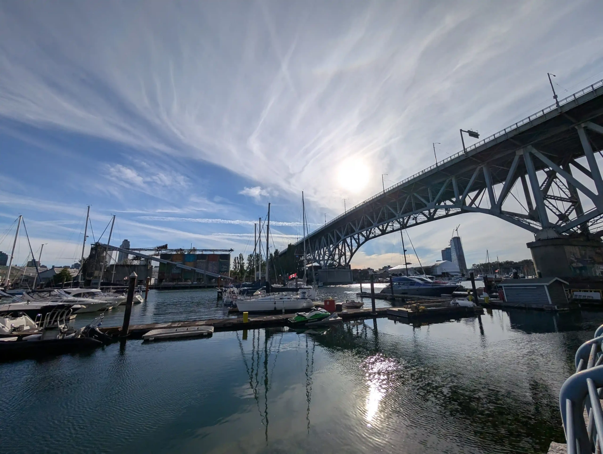 A low-angle view across False Creek marina toward the massive steel superstructure of the Granville Street Bridge, with moored boats.