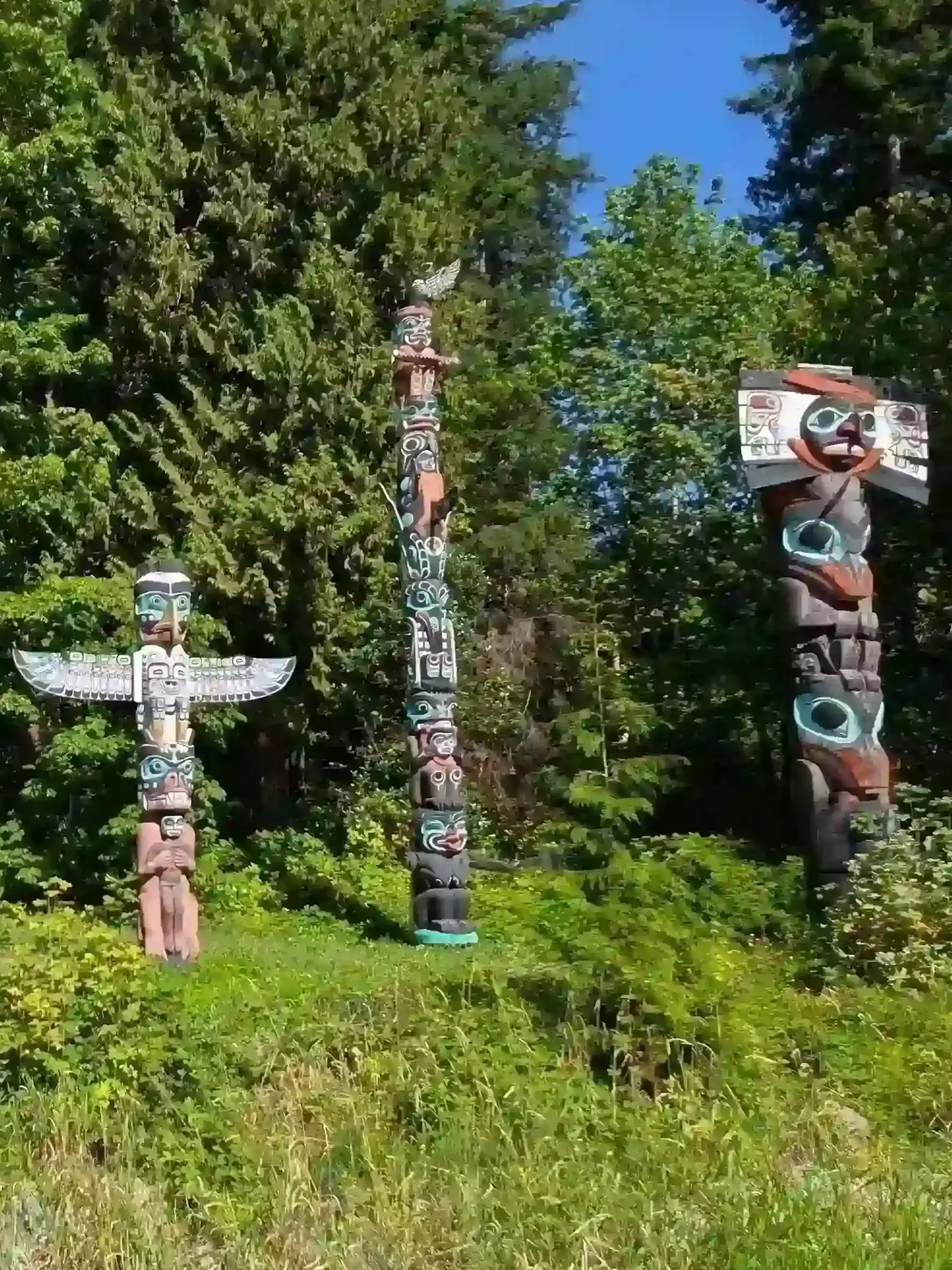 Three wooden totem poles standing on a grassy pitch framed by tall green trees.