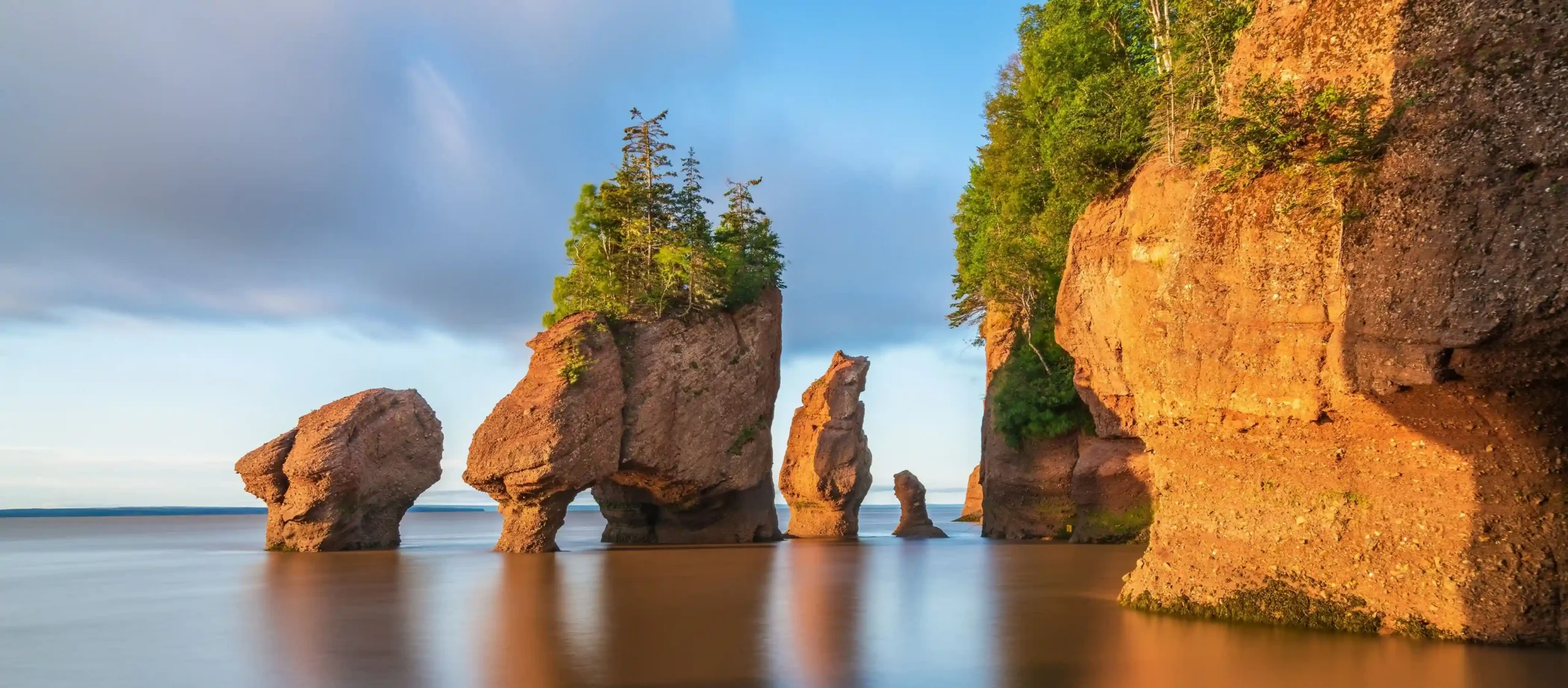 owering, tree-capped rock formations rise from calm, brownish waters during the golden hour.