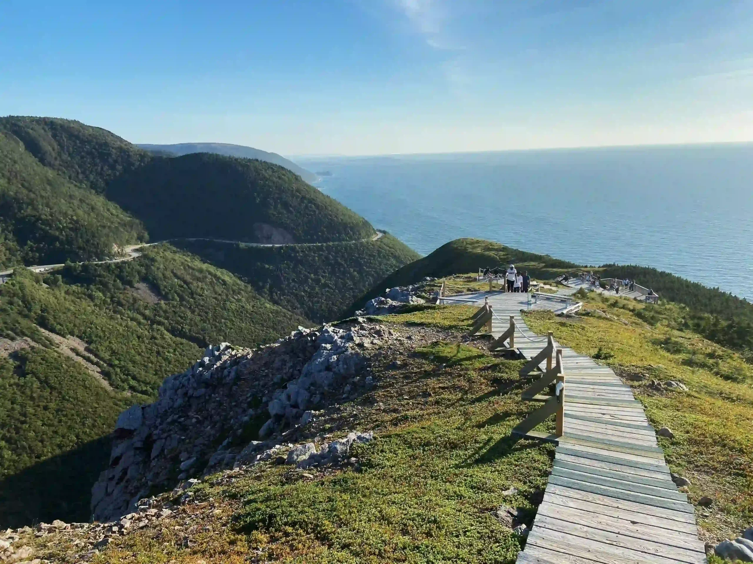 A wooden boardwalk winds down a grassy ridge toward a viewing platform overlooking the Gulf of St. Lawrence.