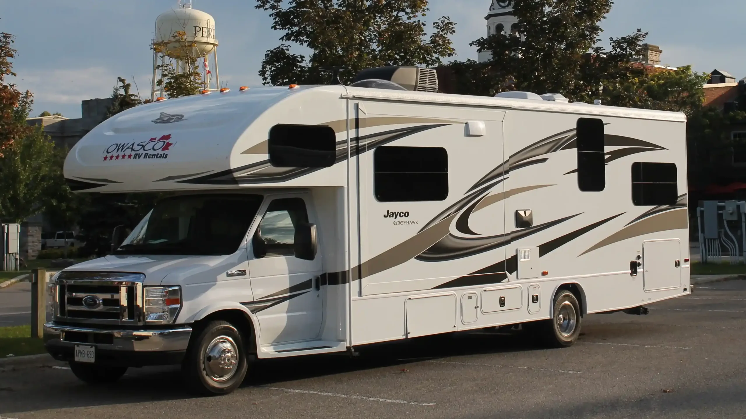A white RV rental parked in a paved lot with a water tower in the background.