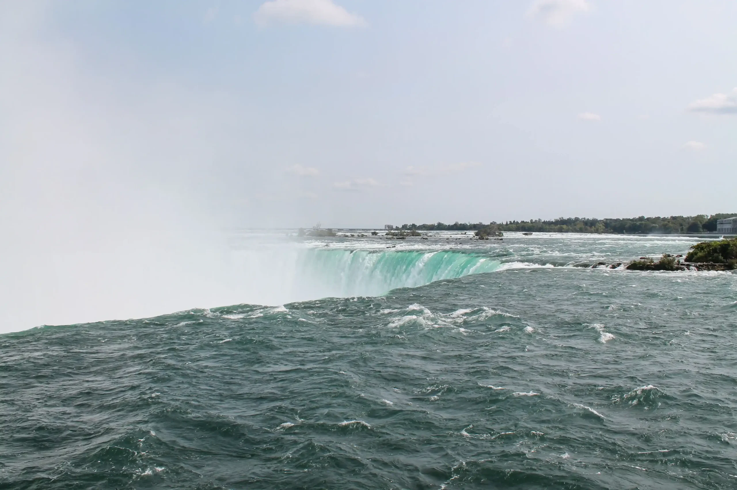 Water rushing over the edge of Niagara Falls, with mist rising above the river below.