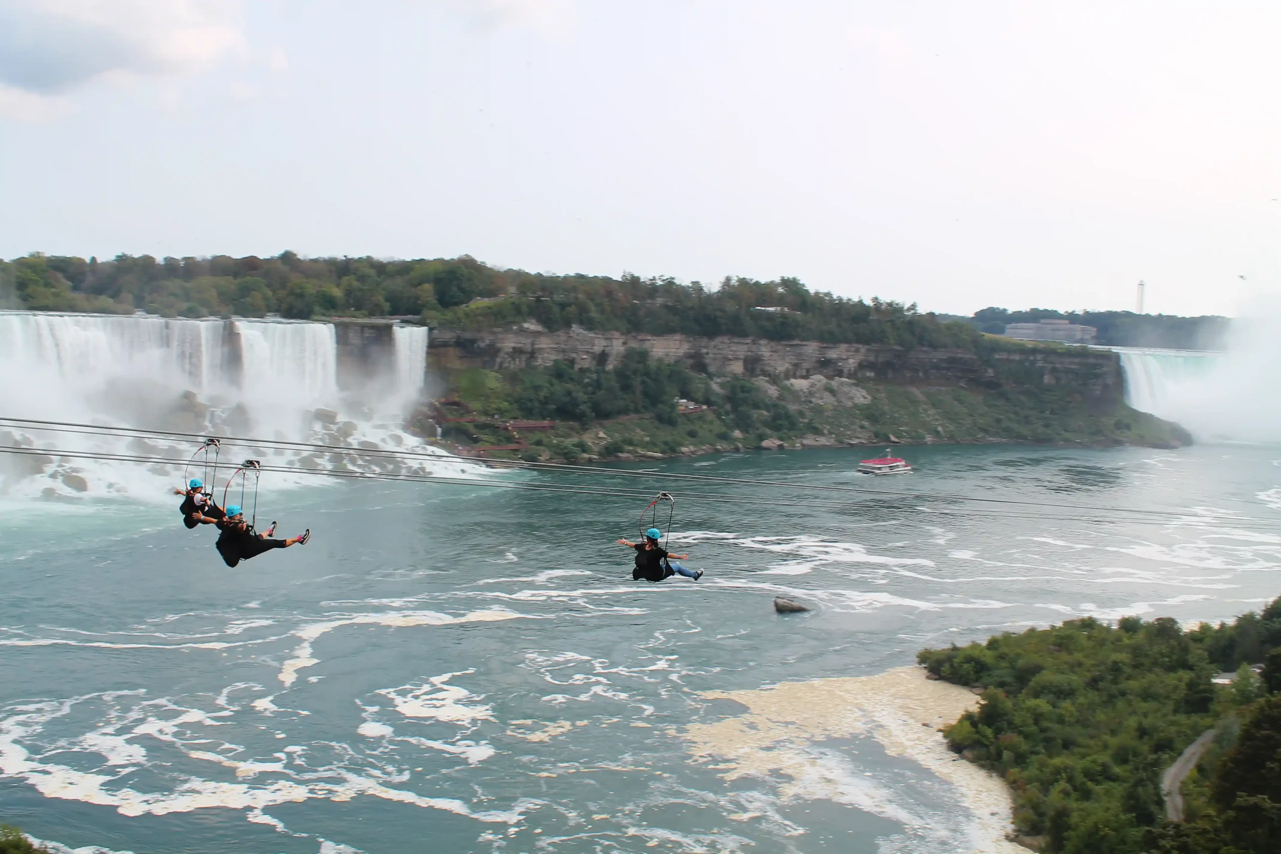 People riding ziplines across the Niagara River with Horseshoe Falls in the background.