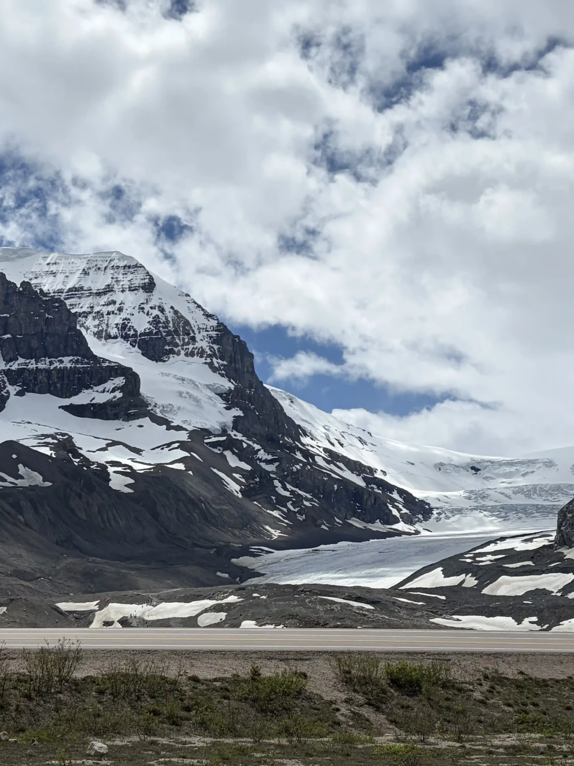 A massive, snow-covered mountain peak and flowing glacier under a dramatic cloudy sky.