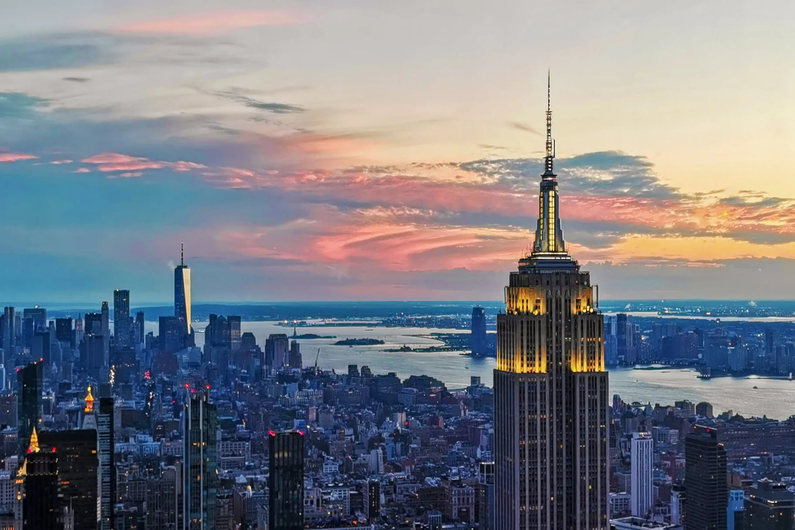 Panoramic view of the New York City skyline at sunset featuring the illuminated Empire State Building.