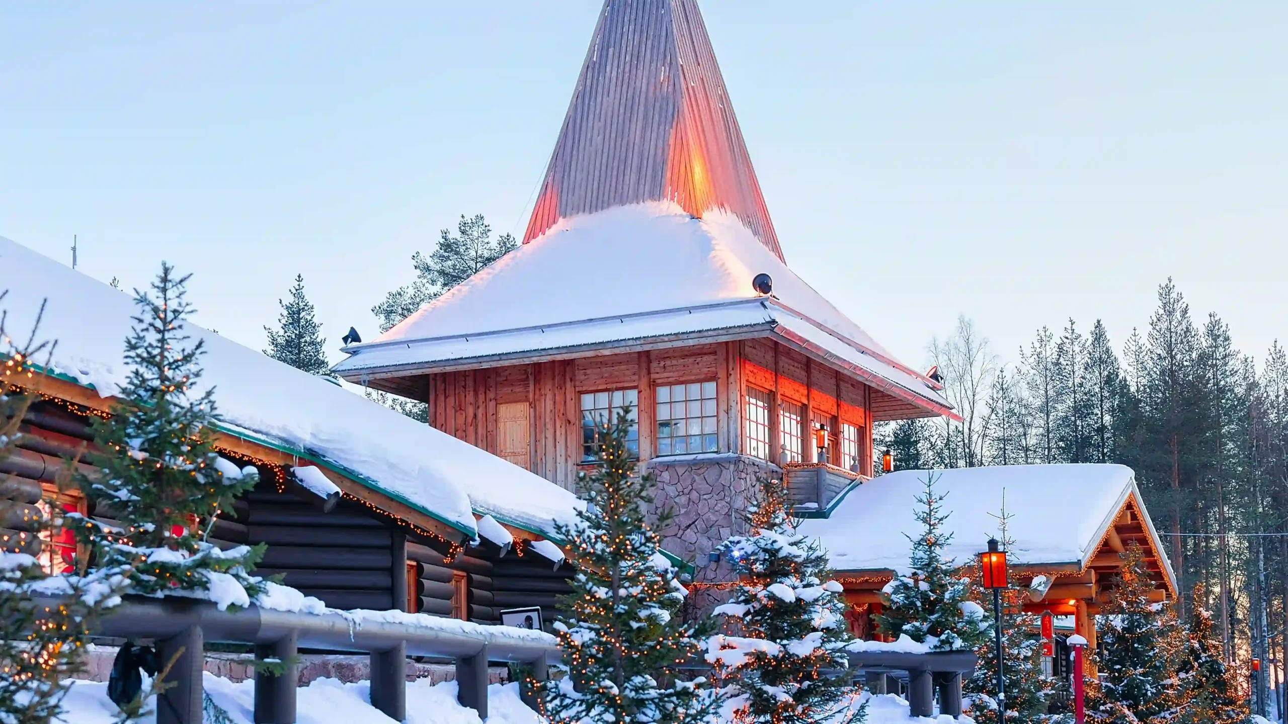 A cozy, snow-covered wooden building with a tall, pointed spire in Santa Claus Village, Lapland.