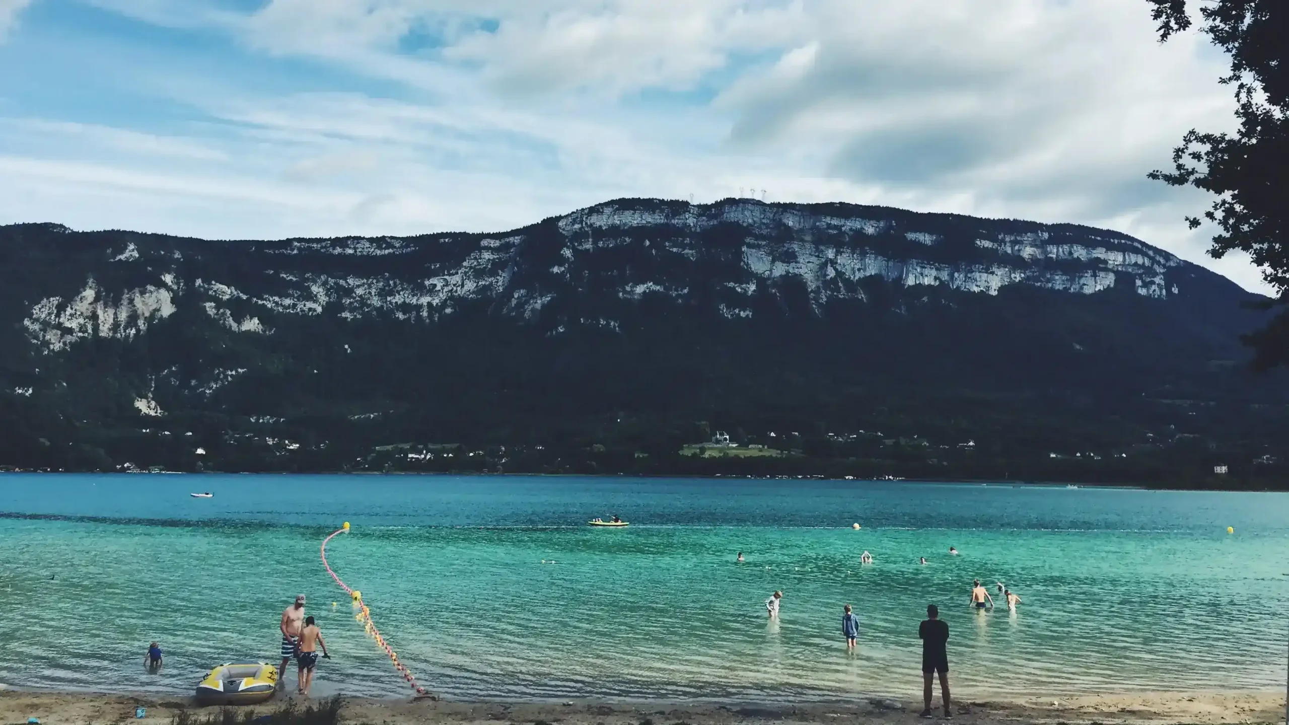 The clear turquoise waters of Lac du Bourget, backed by a steep forested mountain with limestone cliffs.
