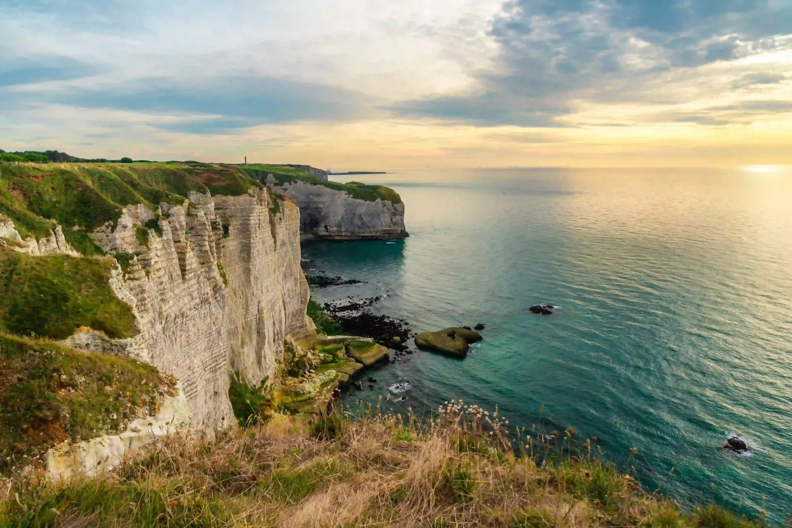 High cliff-edge view looking along steep white chalk cliffs dropping into calm ocean waters.