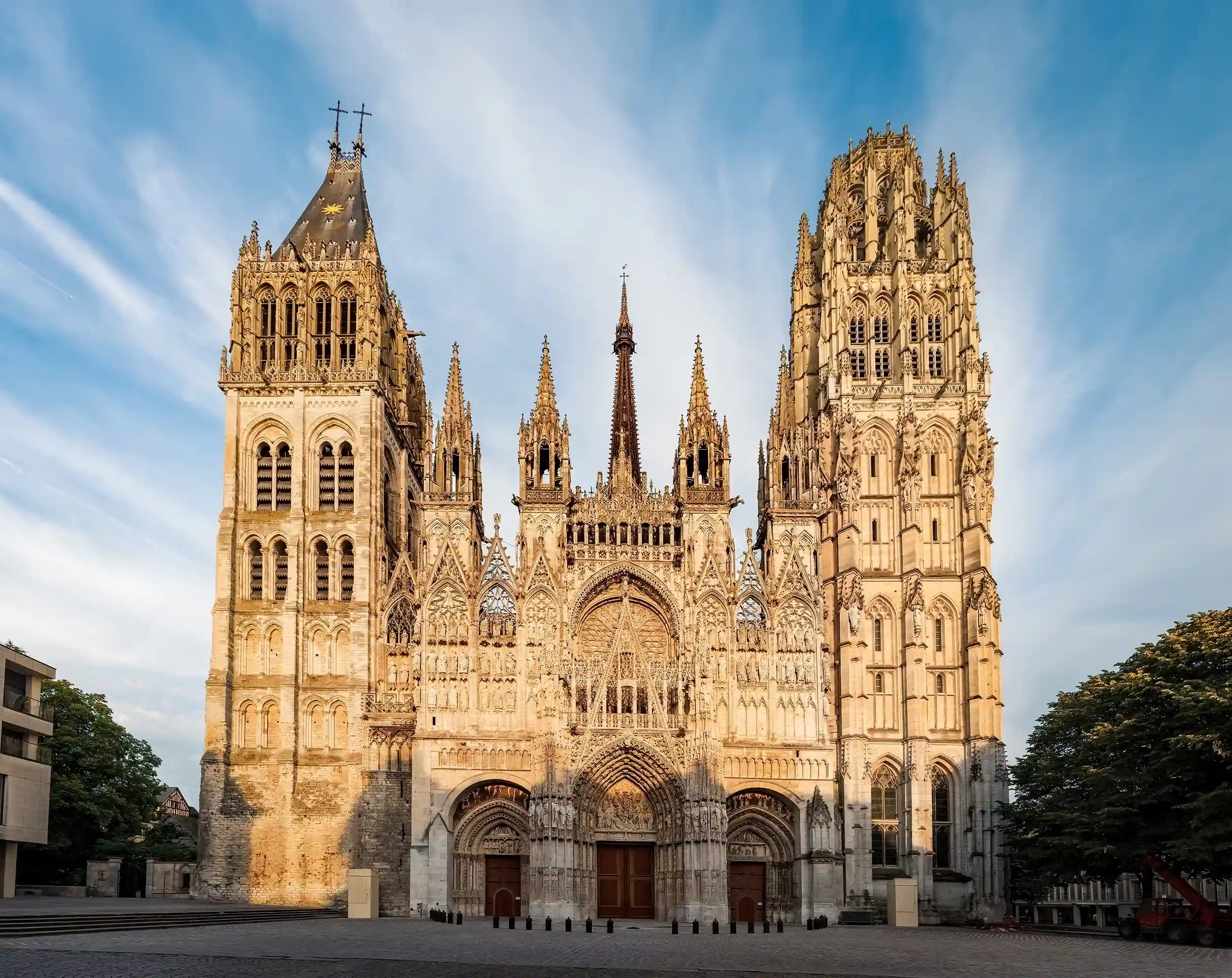 View of the Gothic Rouen Cathedral featuring two intricate towers and carved archways under a blue sky.